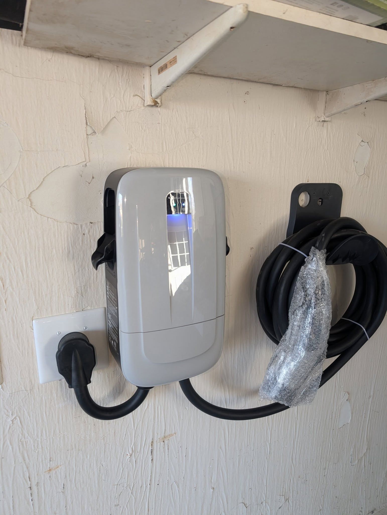 An electric car charger is hanging on a wall next to a shelf.