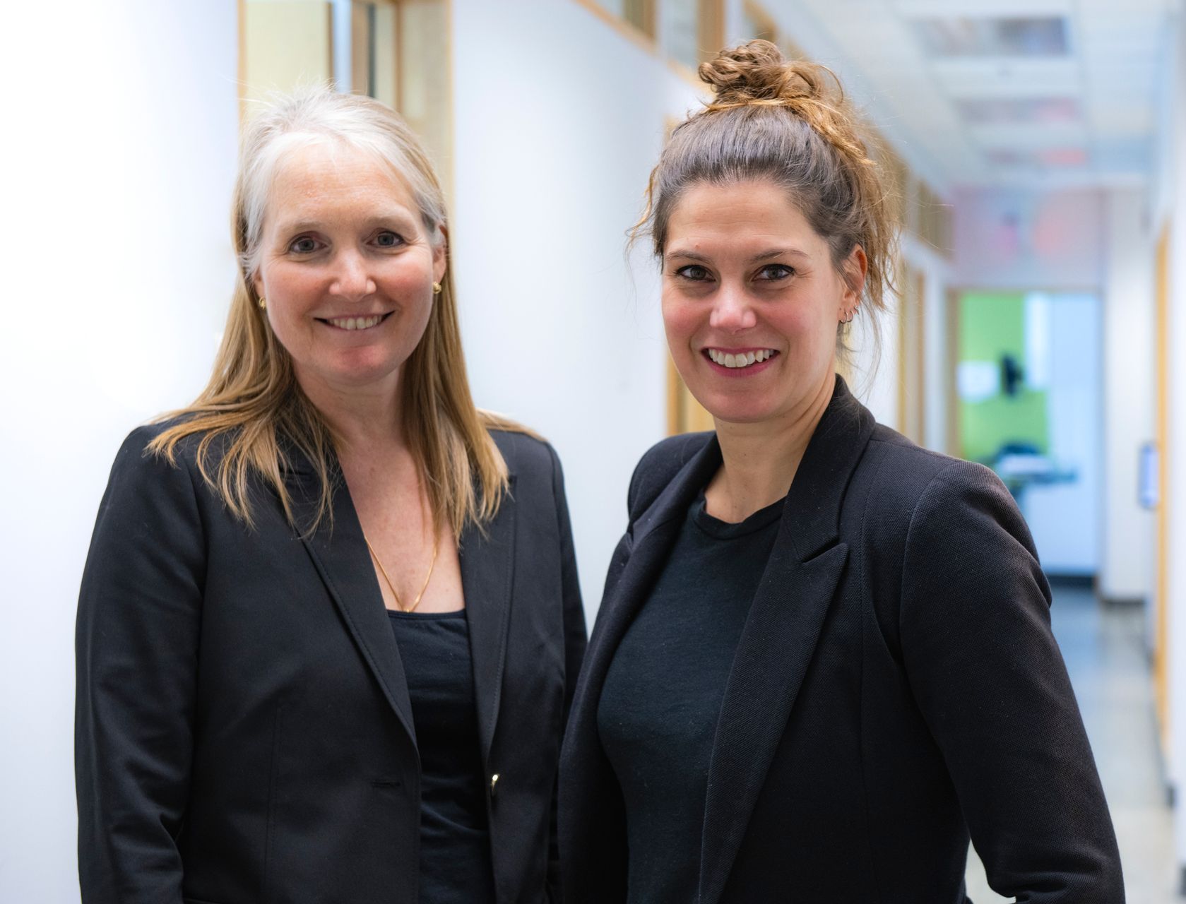Deux femmes se tiennent l'une à côté de l'autre dans un couloir et sourient.