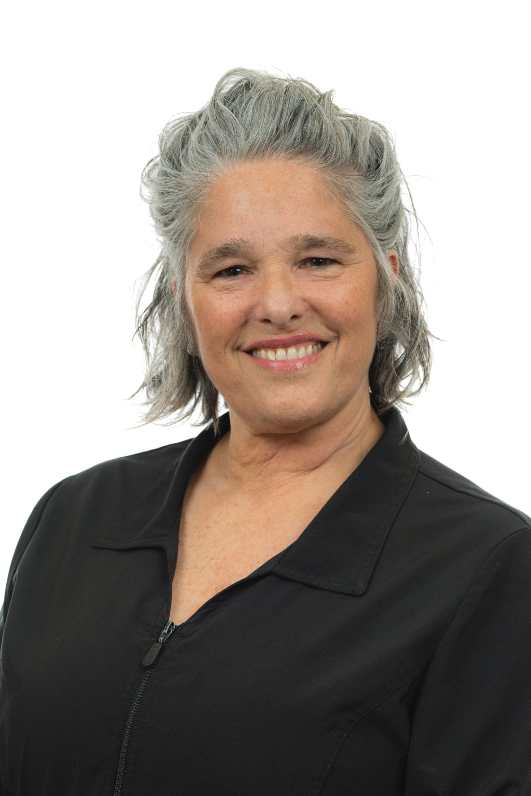Une femme aux cheveux gris et à la veste noire sourit à la caméra.
