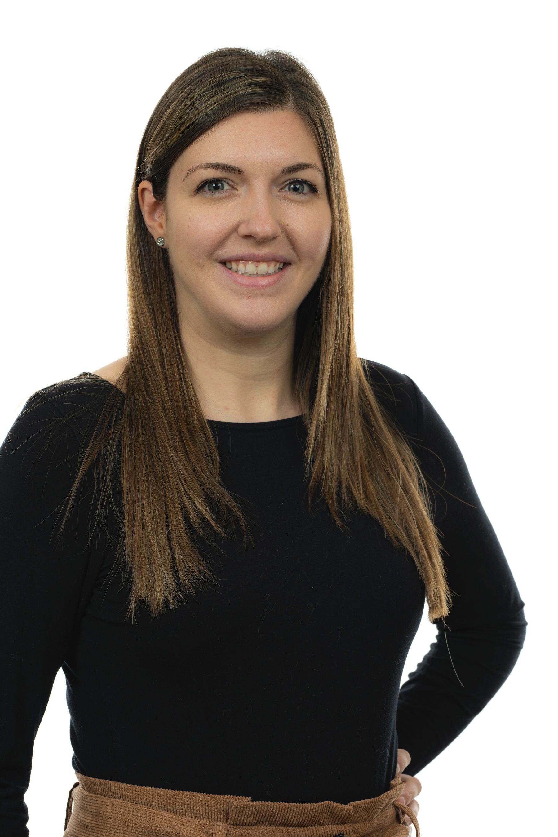 Une femme portant une chemise noire et un pantalon marron sourit à la caméra.
