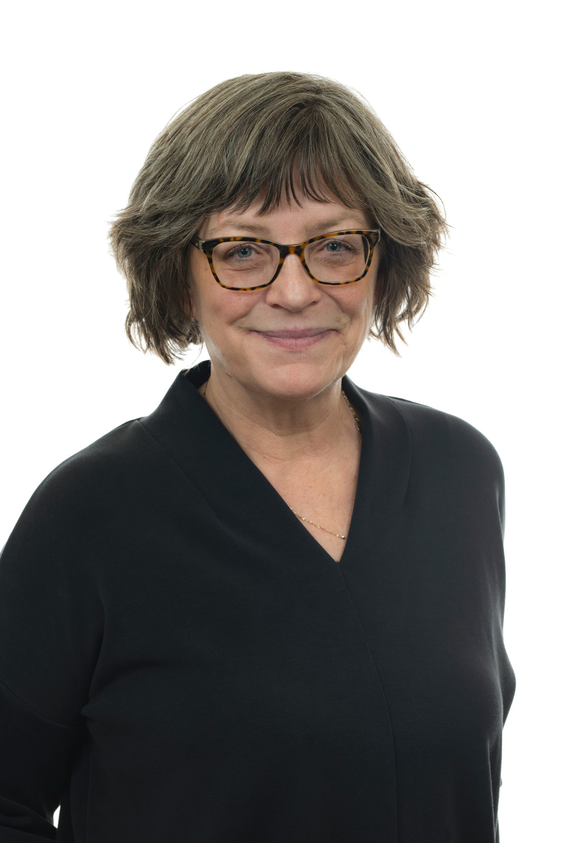 Une femme portant des lunettes et un pull noir sourit à la caméra.