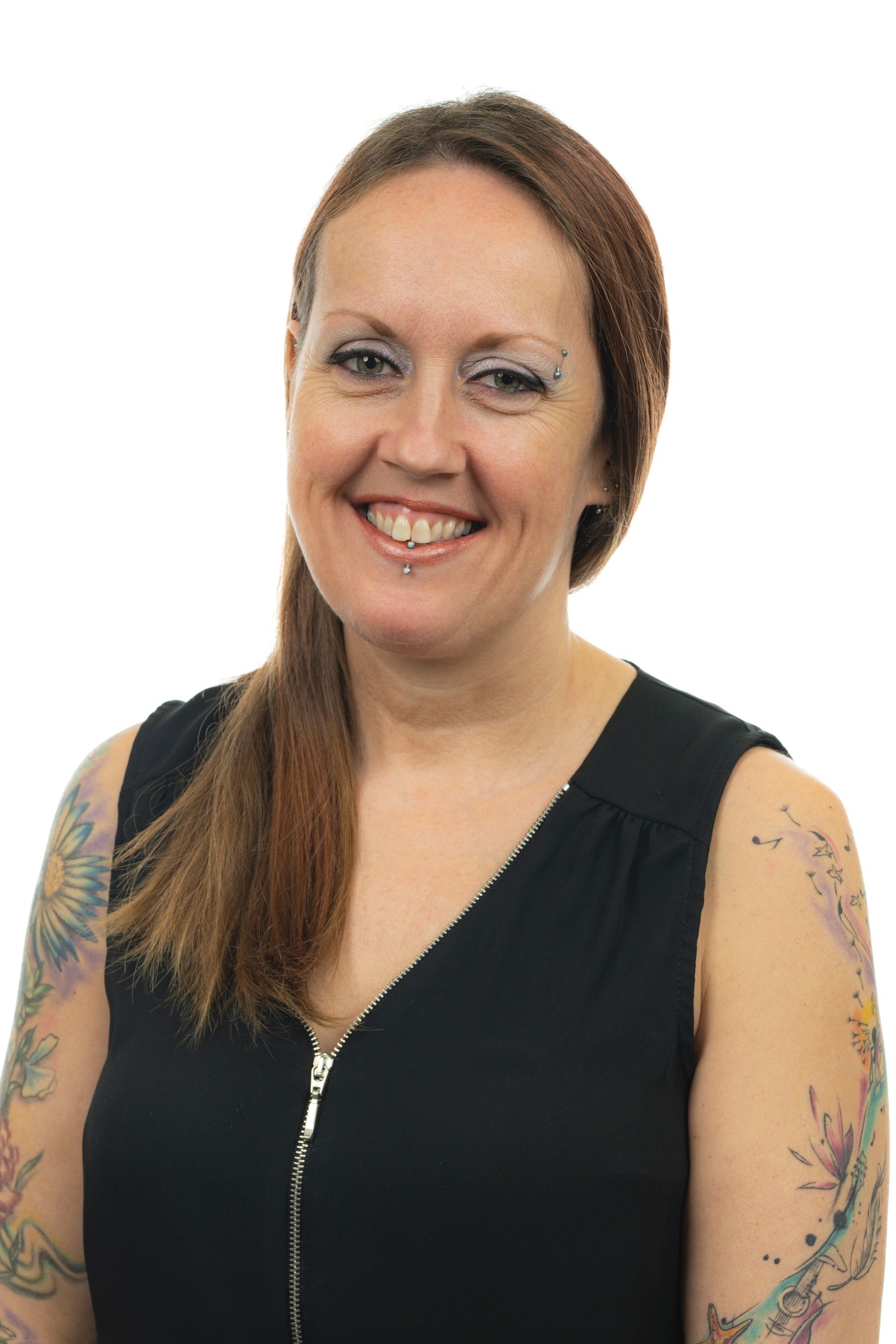 Une femme avec des tatouages ​​sur les bras sourit à la caméra.