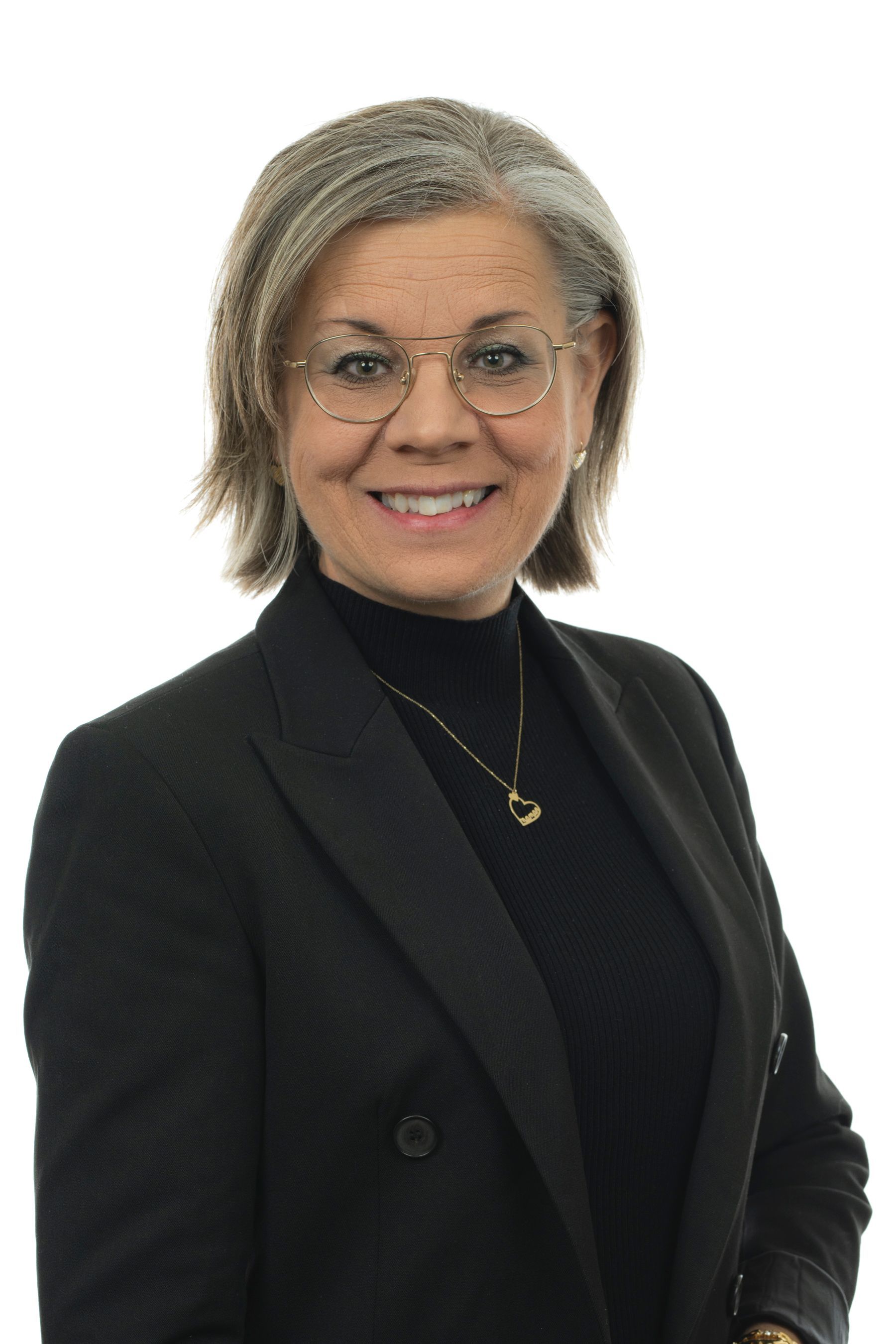 Une femme portant des lunettes et une veste noire sourit à la caméra.