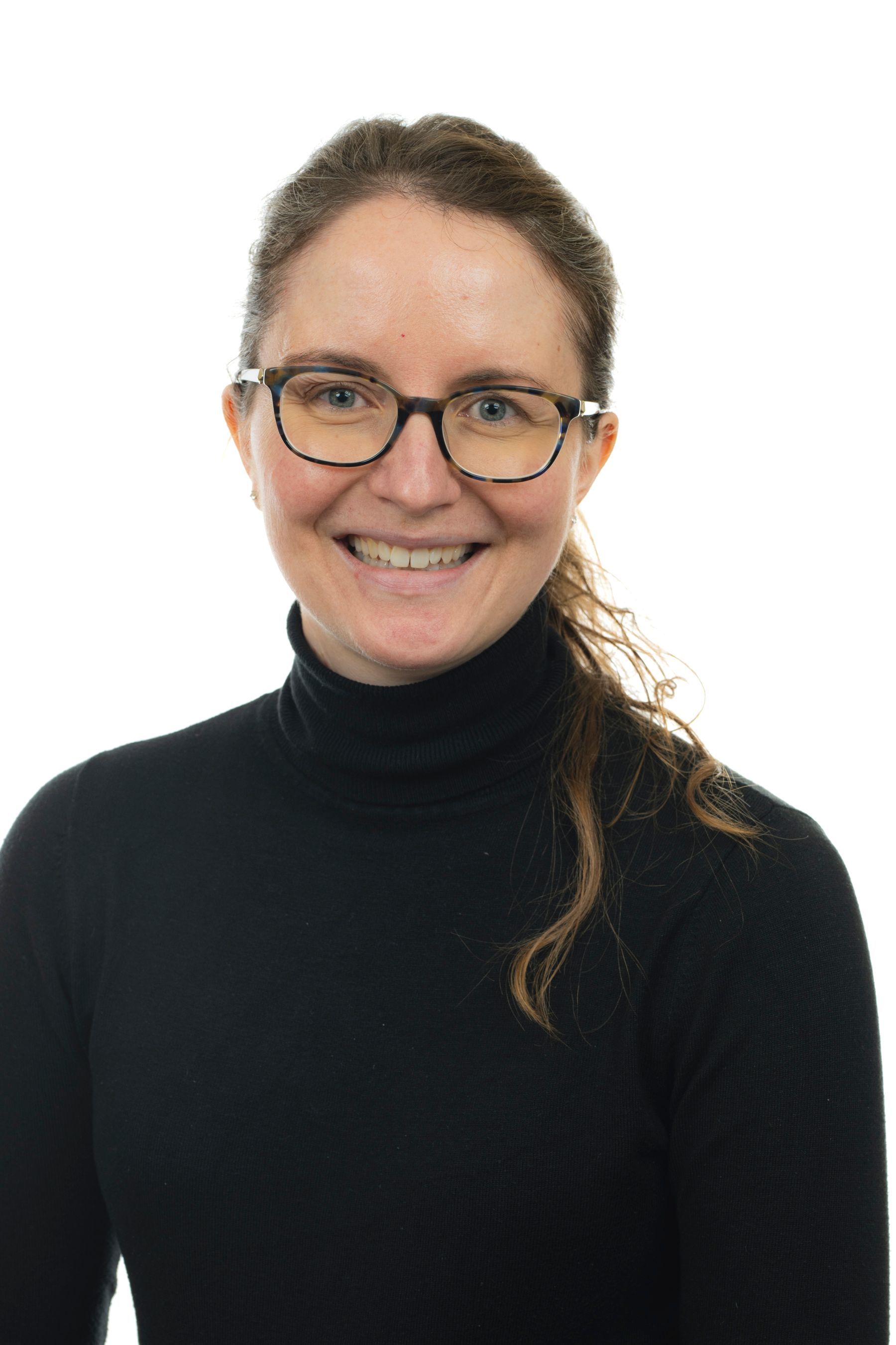 Une femme portant des lunettes et un col roulé noir sourit à la caméra.