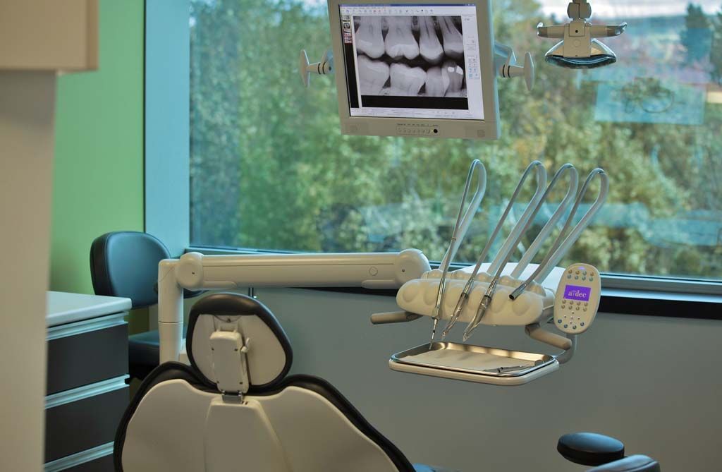 Un cabinet dentaire avec un fauteuil dentaire et un moniteur.