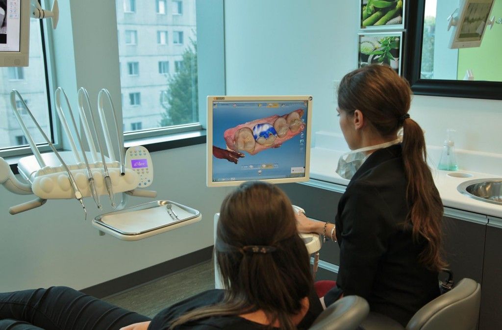Une femme est assise sur une chaise dentaire et regarde un écran d'ordinateur.