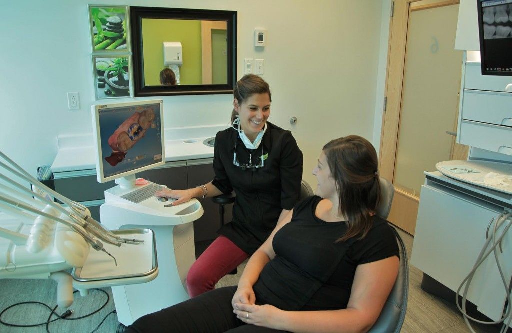 Une femme est assise sur une chaise dentaire et parle à un dentiste.