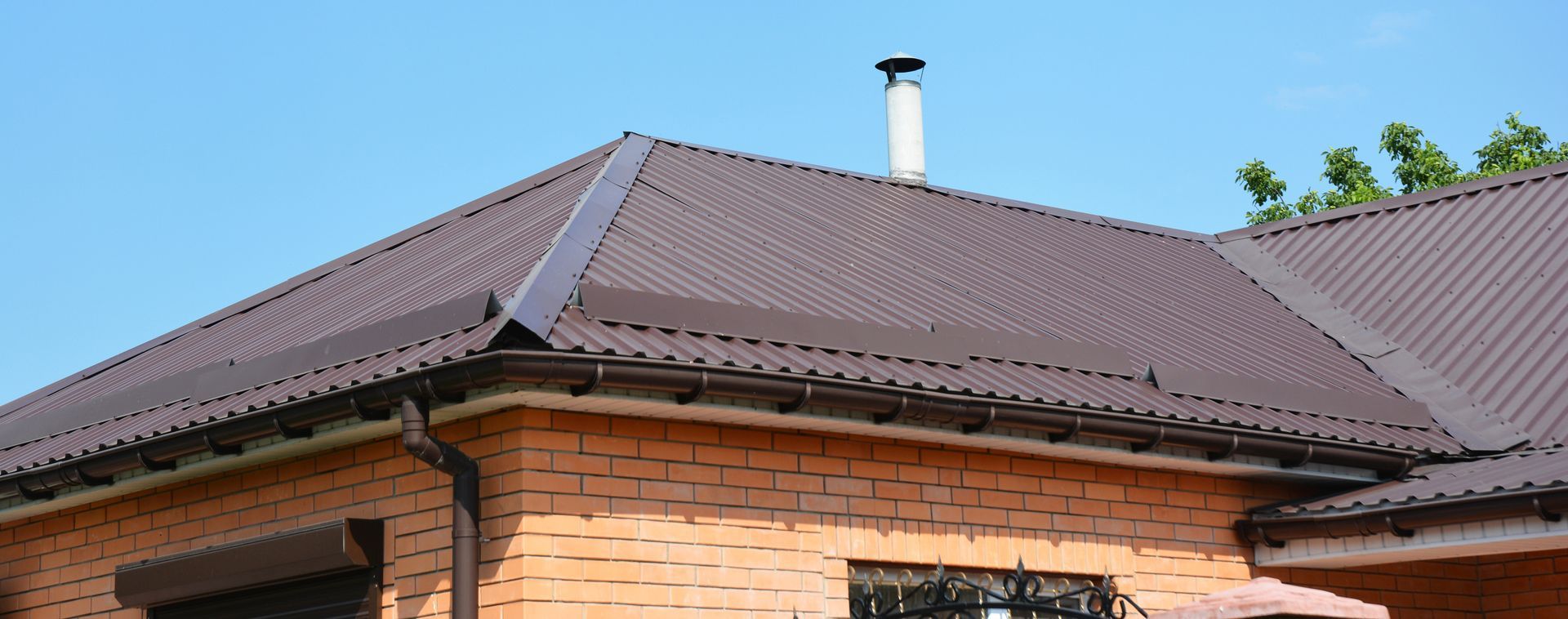 Brown roof of a brick house with a chimney and blue sky.