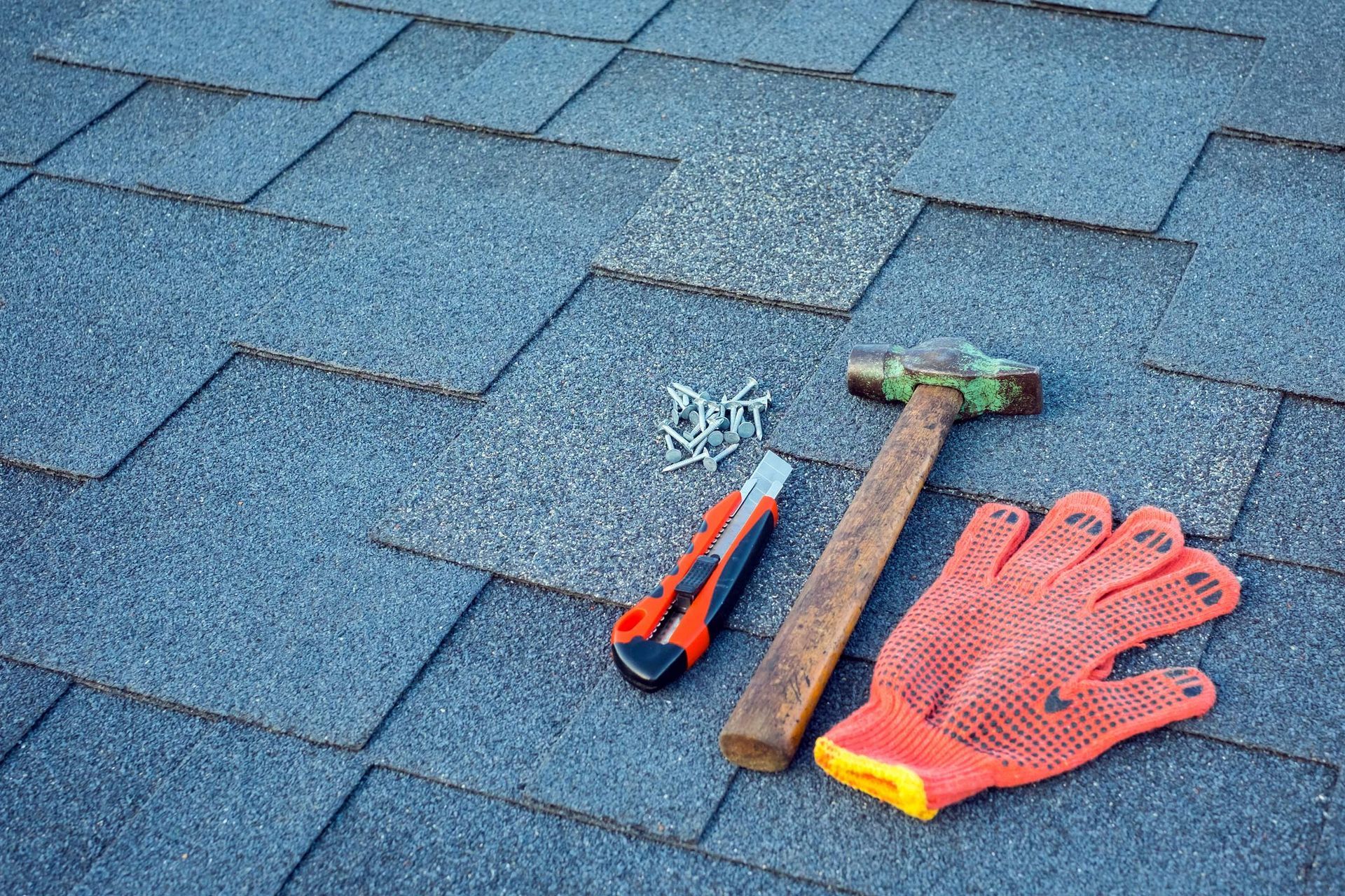 Close-up view of shingles on a roof with a hammer, nails, and a stationery knife.