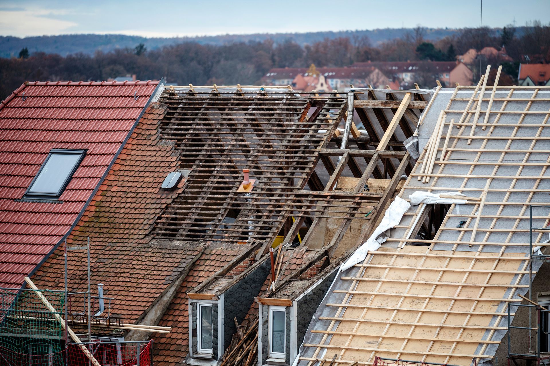 Workers replacing roof tiles on a house, with some roofs partially stripped