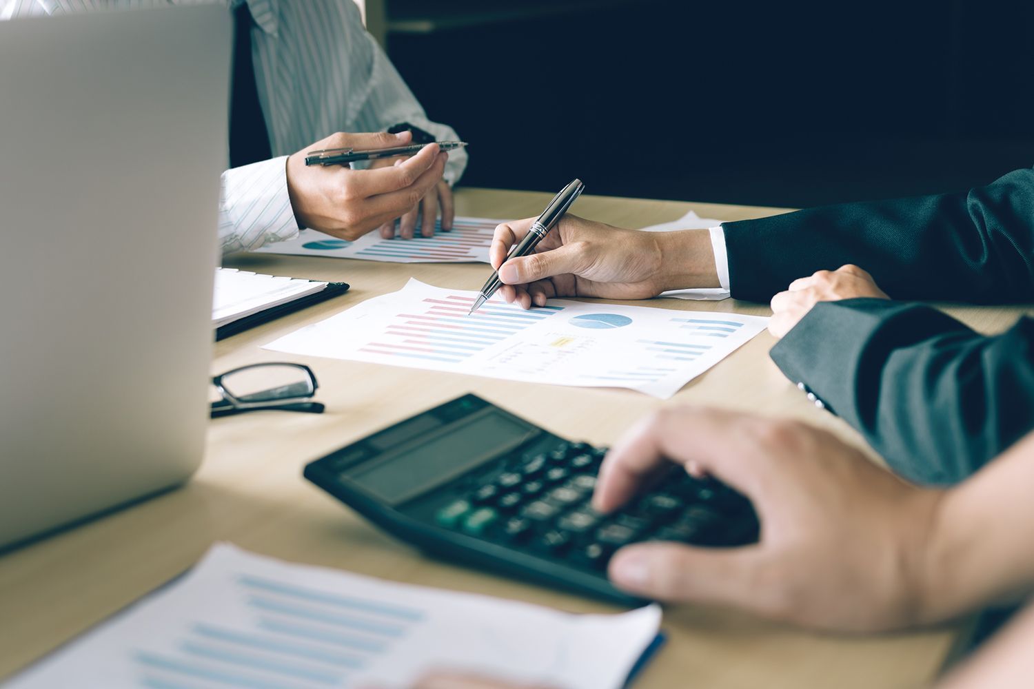 Business people reviewing financial data with a calculator and laptop on a desk.