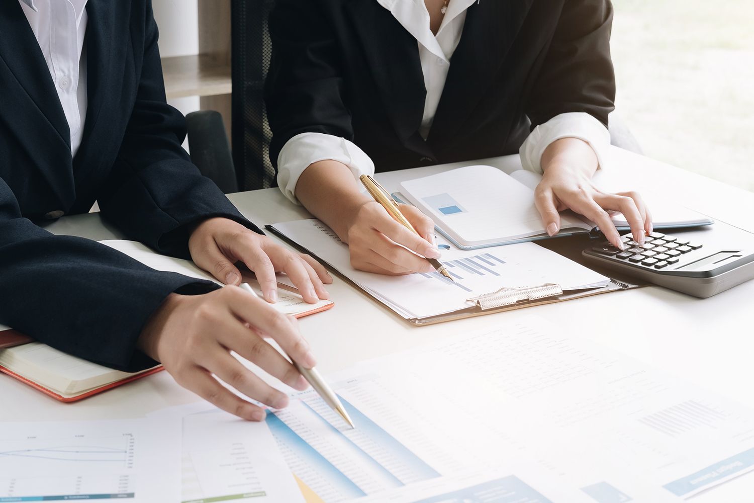 Two people in business attire at a table, reviewing documents, using a calculator and pen.