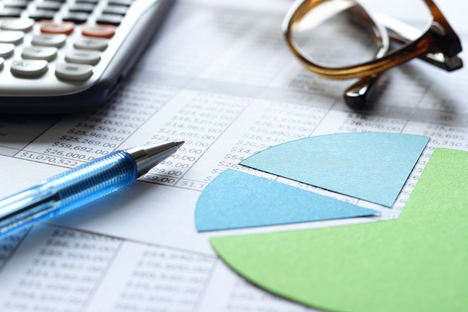 Calculator, pen, glasses, and pie chart on a financial spreadsheet.