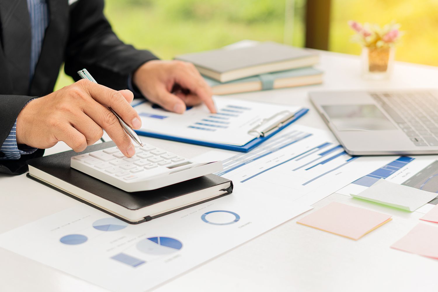 Person in suit calculating with calculator, reviewing financial reports in office setting.