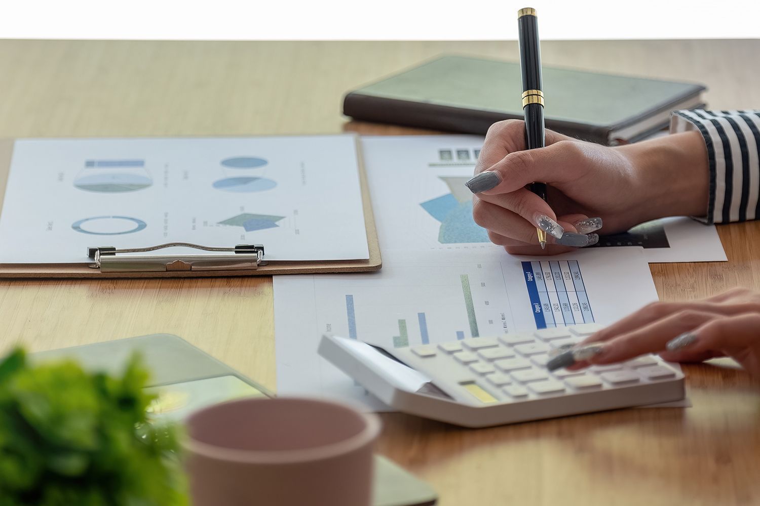 Woman's hands calculating on a calculator, writing on charts, and working at a desk.