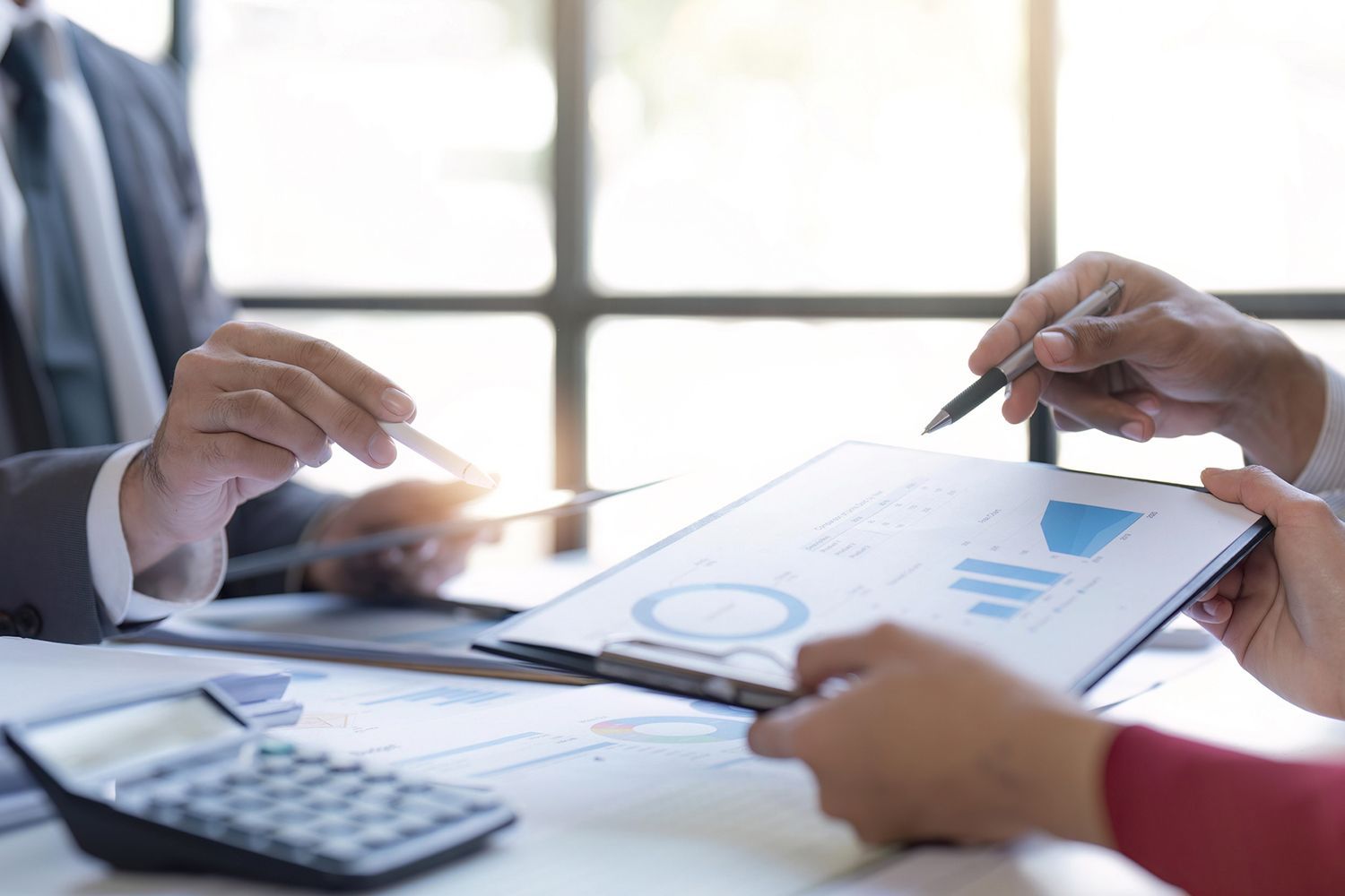 Business meeting with charts and calculator. People in suits review data, pointing at paperwork.