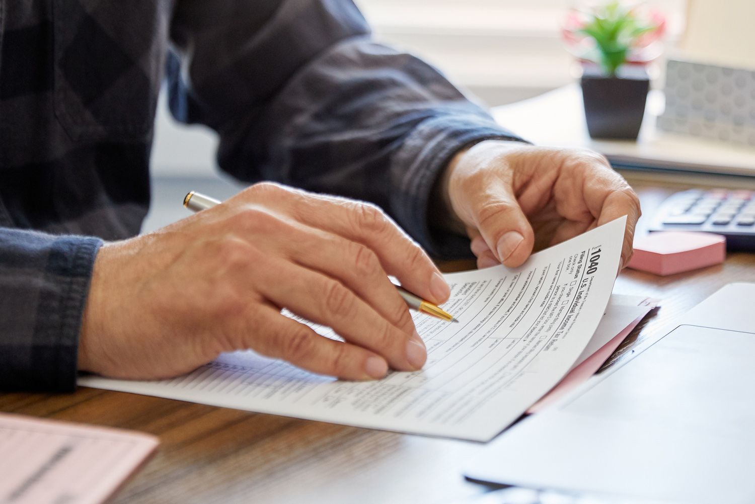 Person reviewing paperwork with a pen in hand at a desk, possibly reviewing a document.