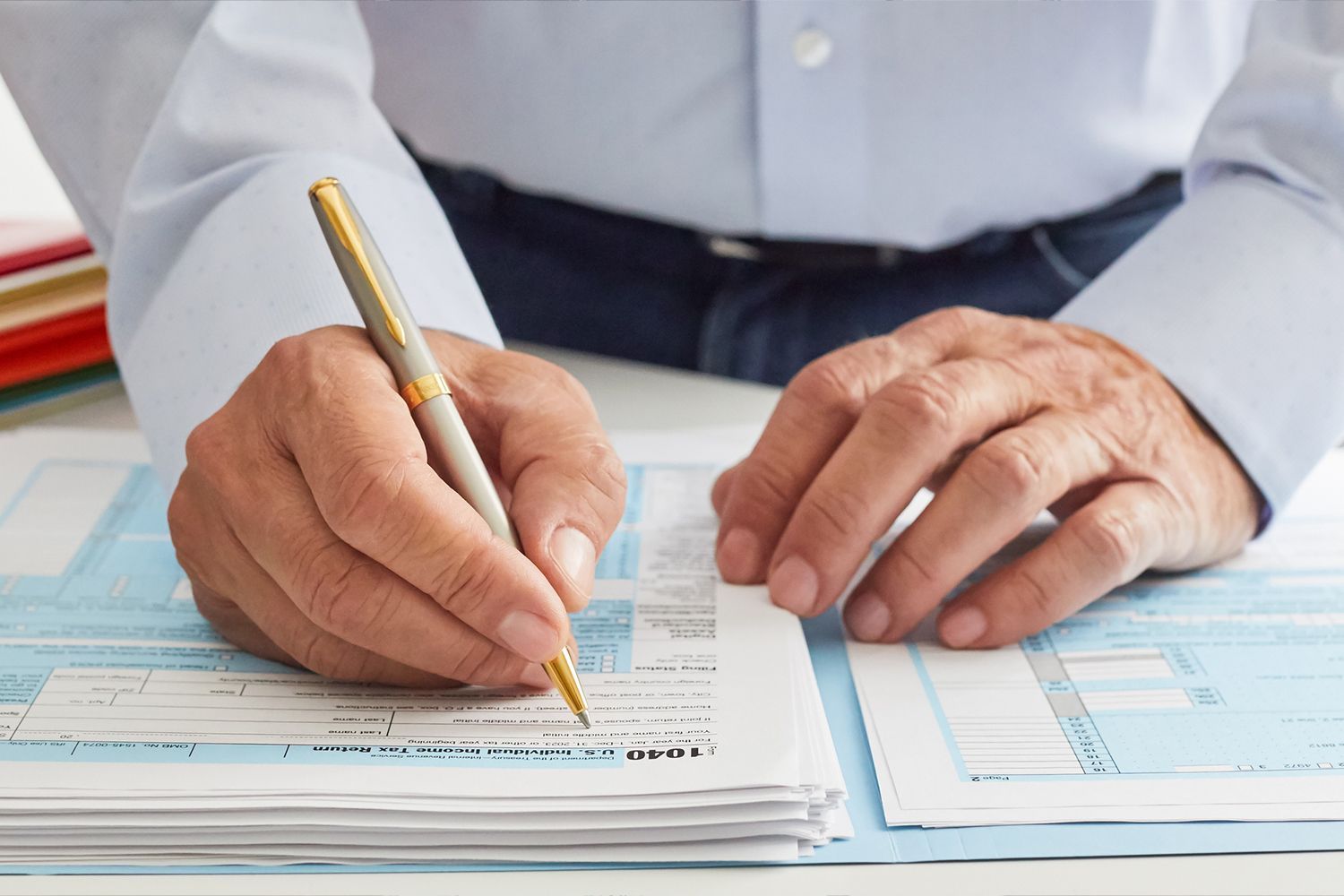 Person filling out tax forms with a pen, seated at a desk.