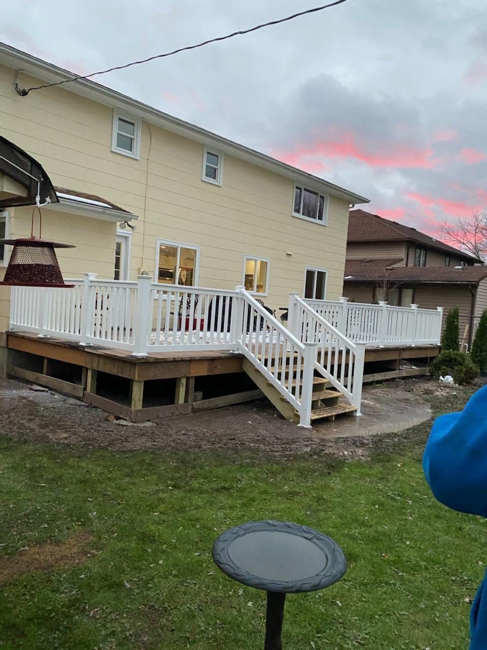 Backyard deck with white railings and stairs beside a beige house under a cloudy pink sky