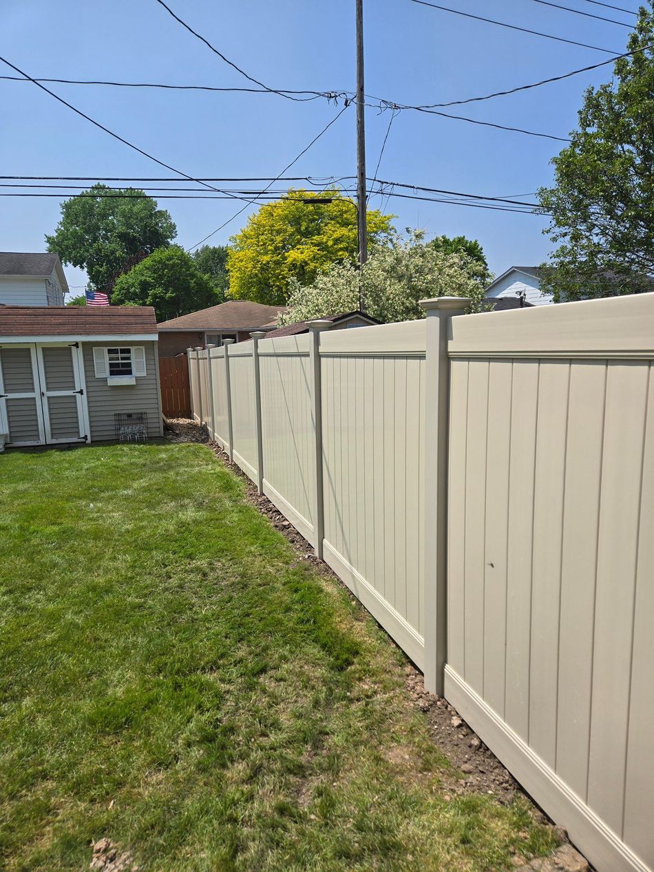 Backyard with beige fence, grassy lawn, shed, and blue sky with overhead power lines