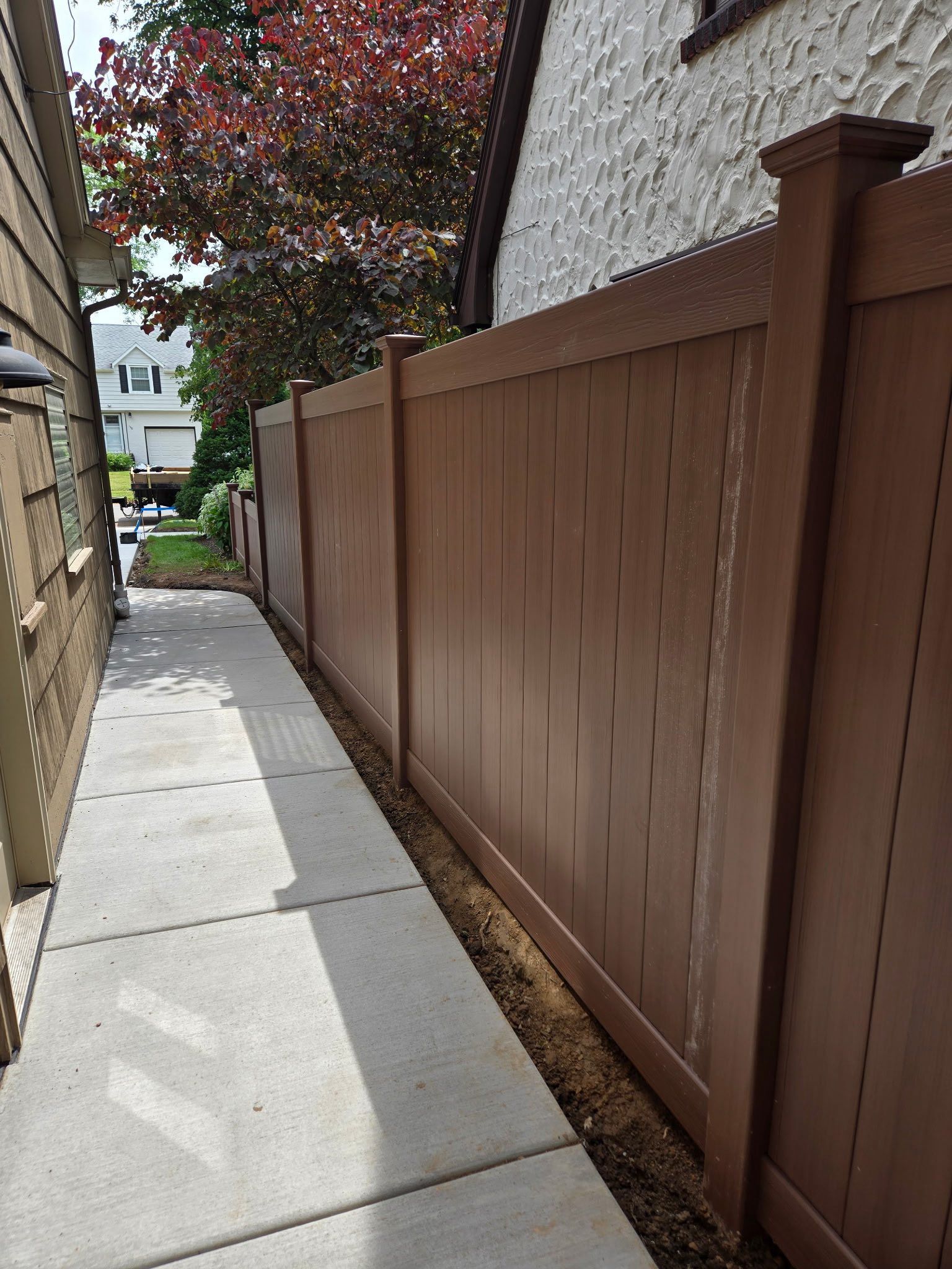 Narrow concrete sidewalk beside a brown wooden fence along a residential building