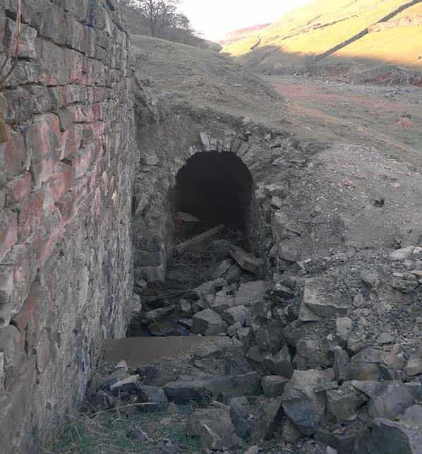 A stone tunnel entrance built into a rocky hillside, with scattered rubble in the foreground.