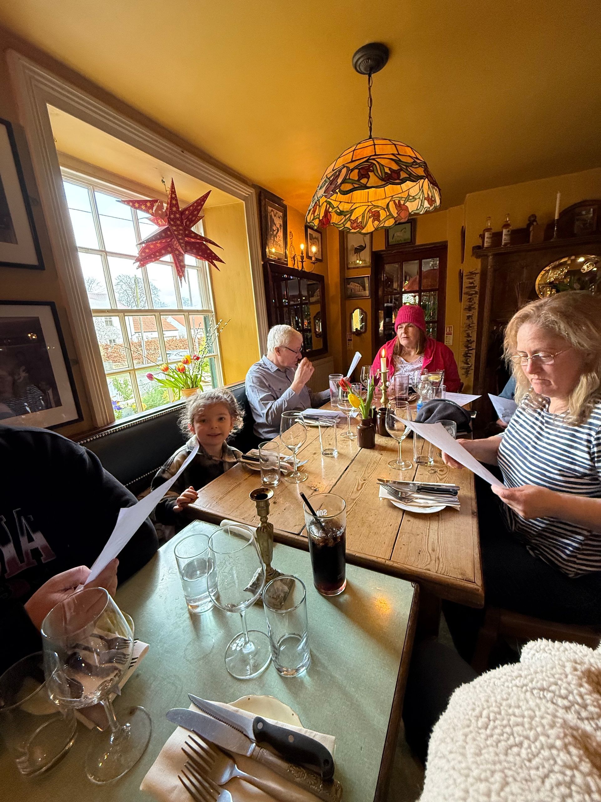 People seated around a rustic wooden table in a dimly lit restaurant, holding papers and preparing to eat.