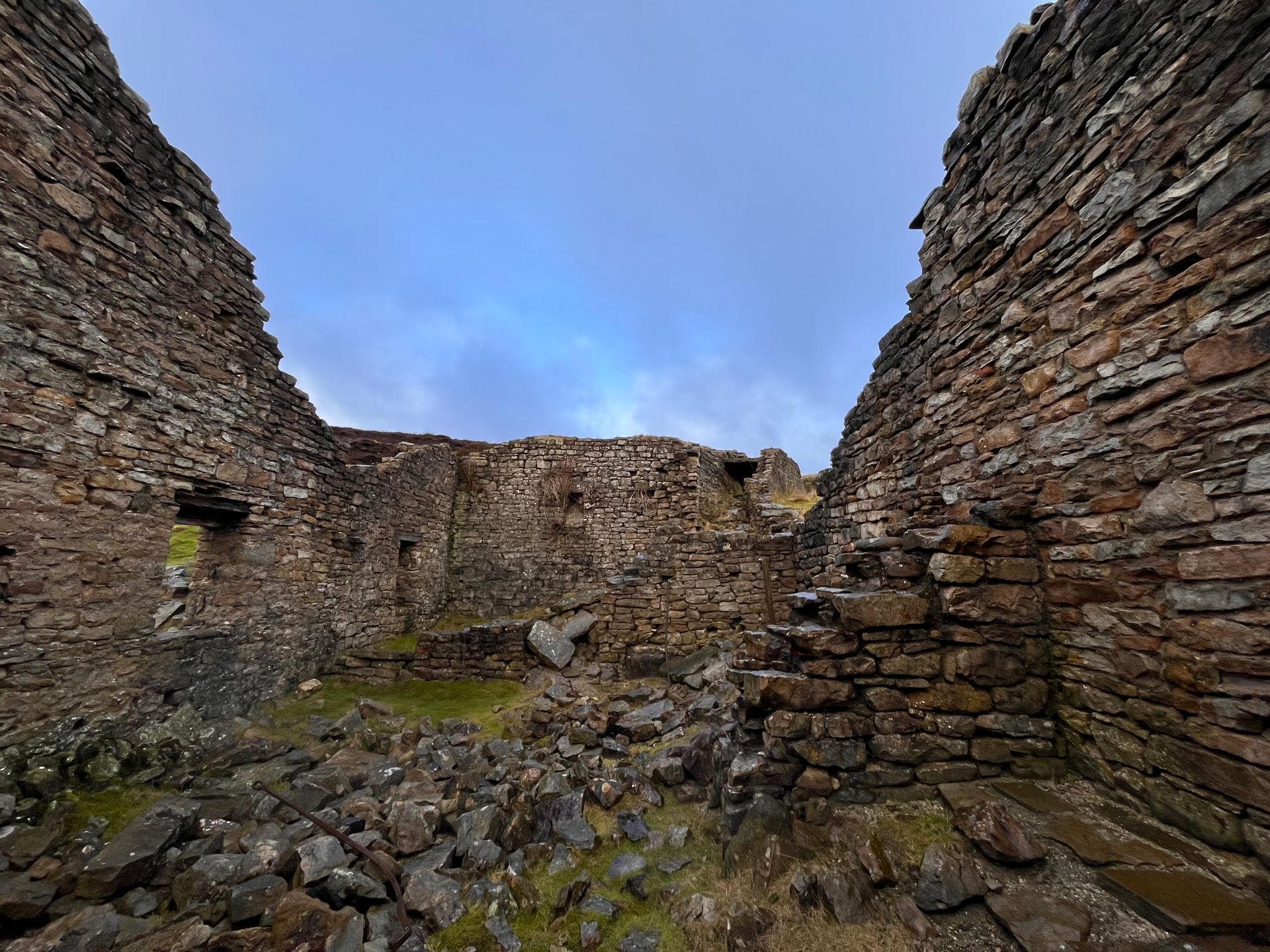 A stone wall with a blue sky in the background is surrounded by rocks.