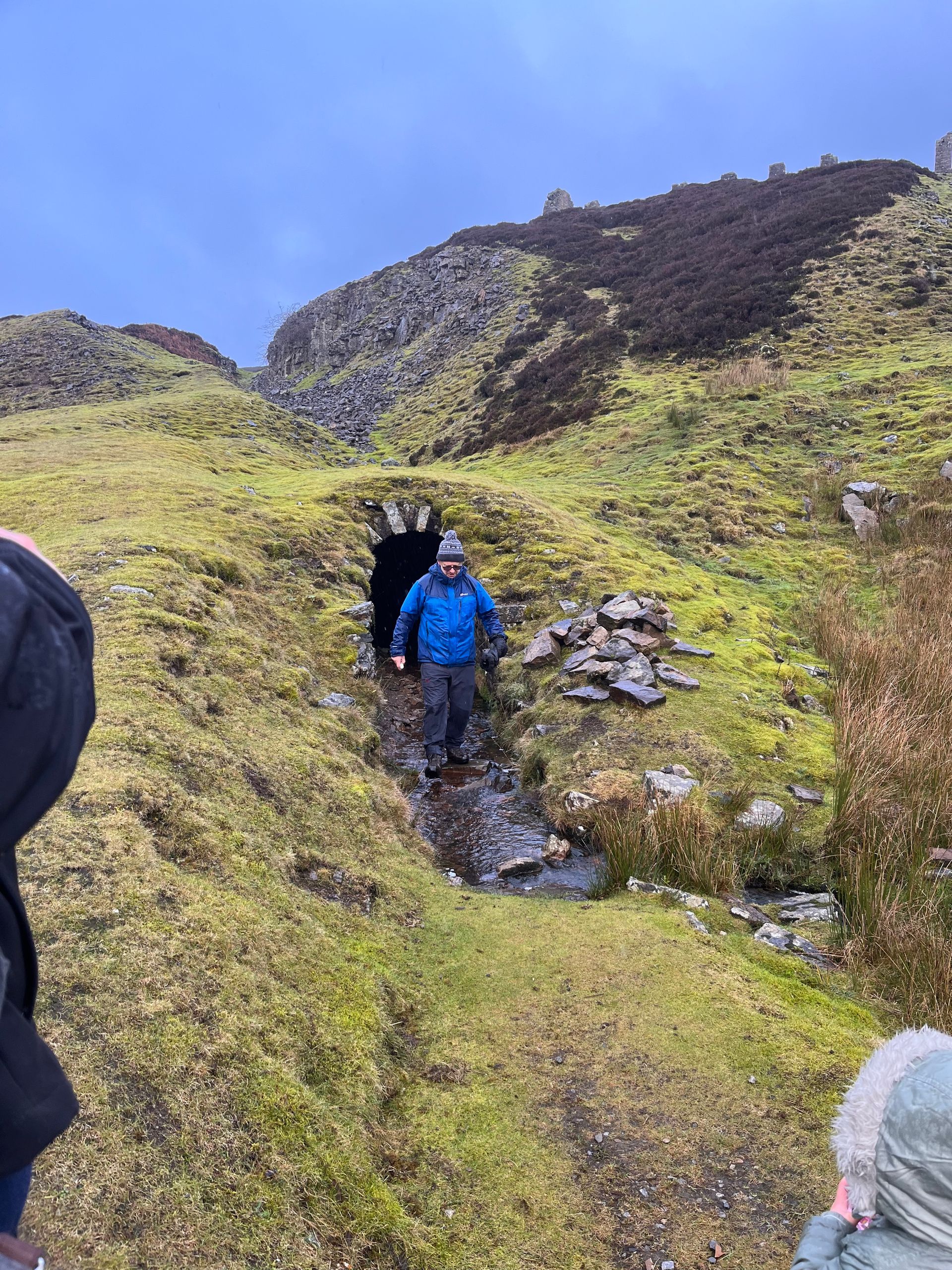 A man in a blue jacket is walking through a tunnel on a hill.