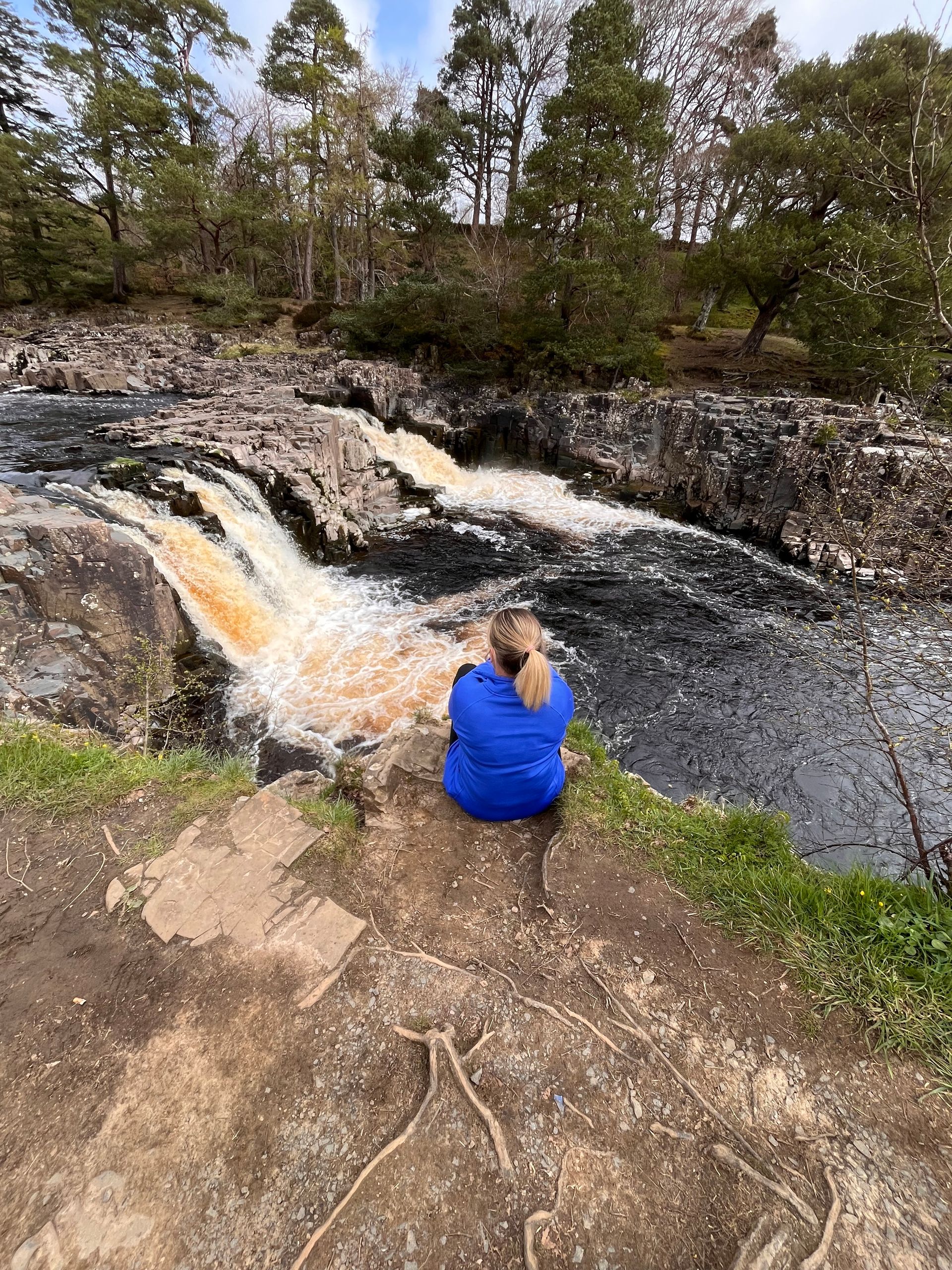 A woman is sitting on the edge of a waterfall looking at the water.