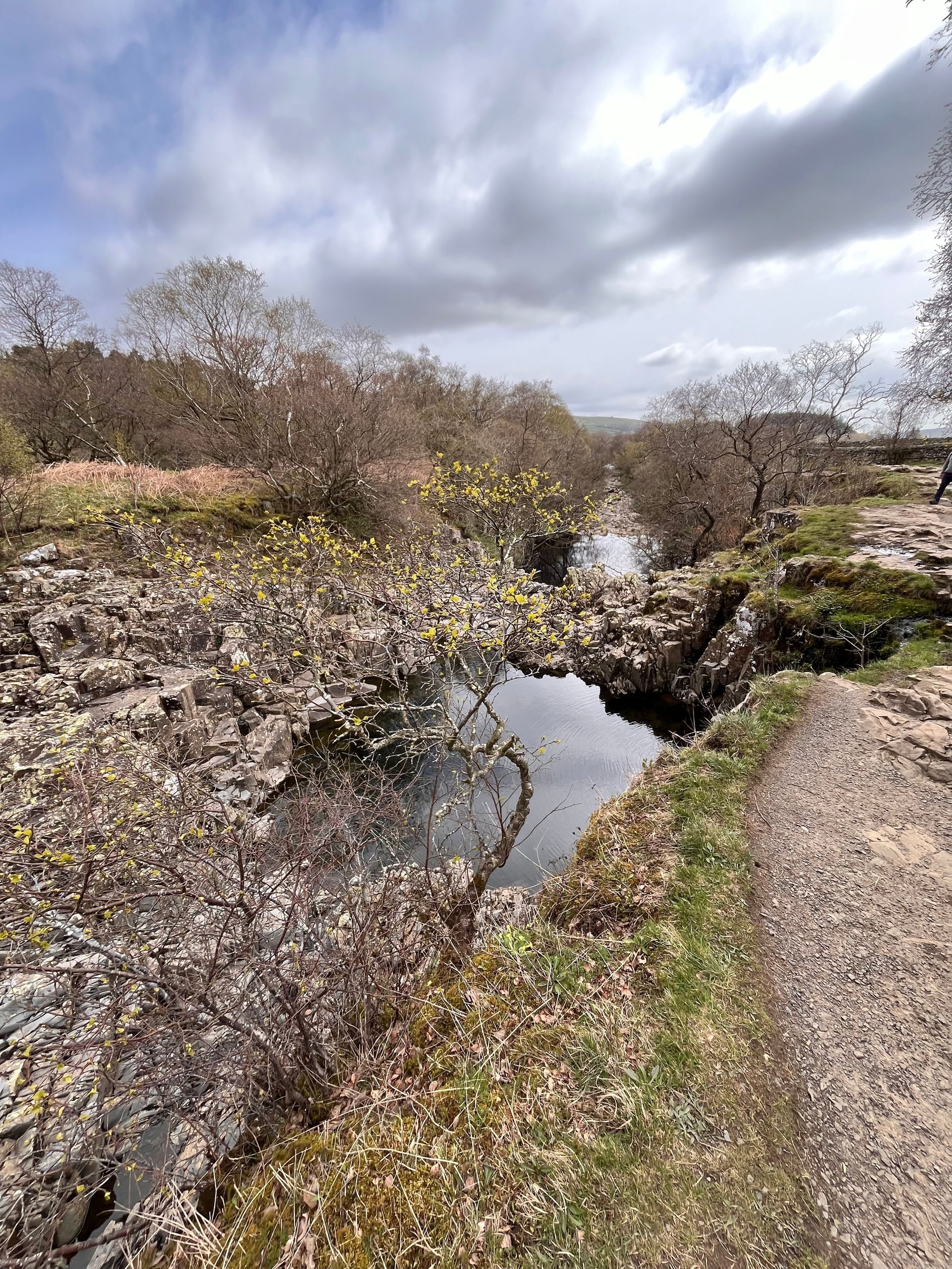 A river runs through a rocky area next to a dirt path.