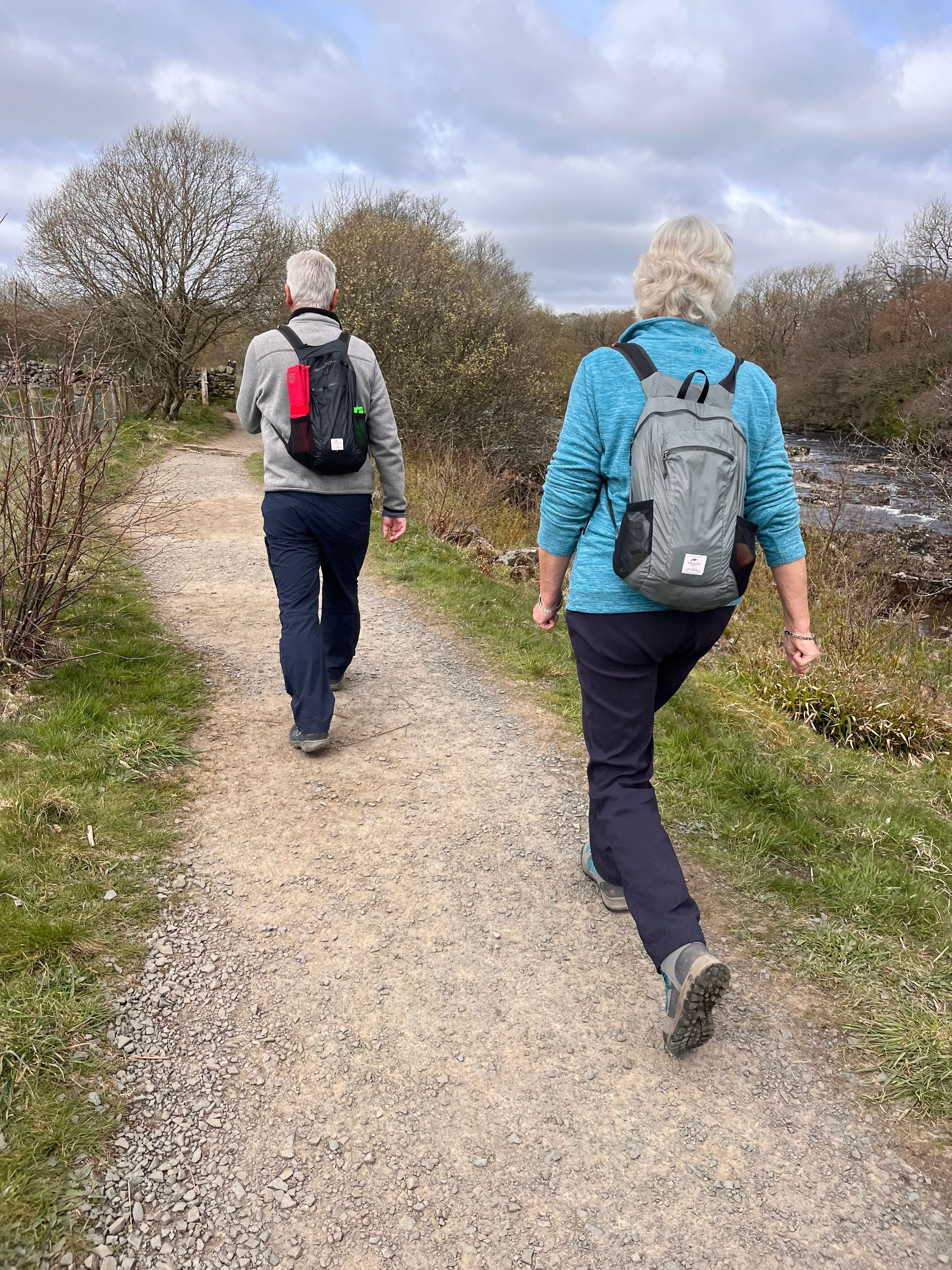 Two people with backpacks are walking down a dirt path.