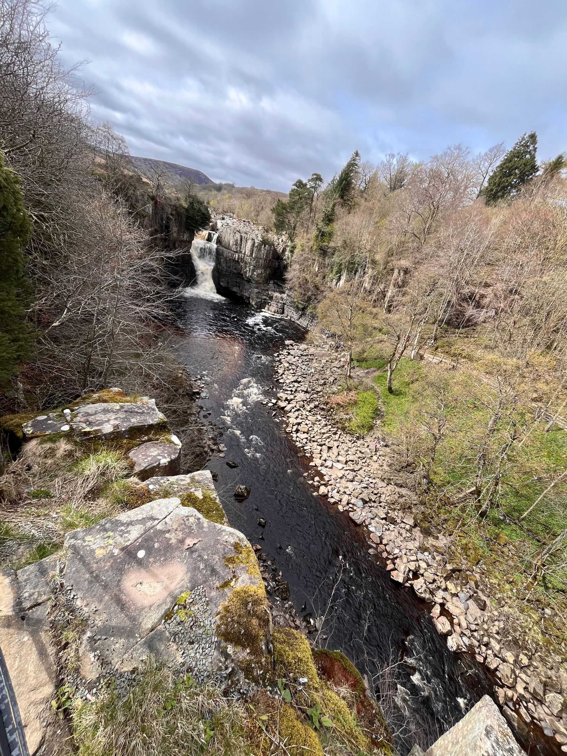 A river flowing through a rocky area with a waterfall in the background.