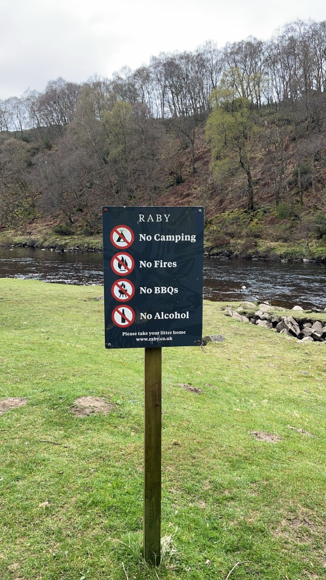 A sign on a wooden post in front of a river.