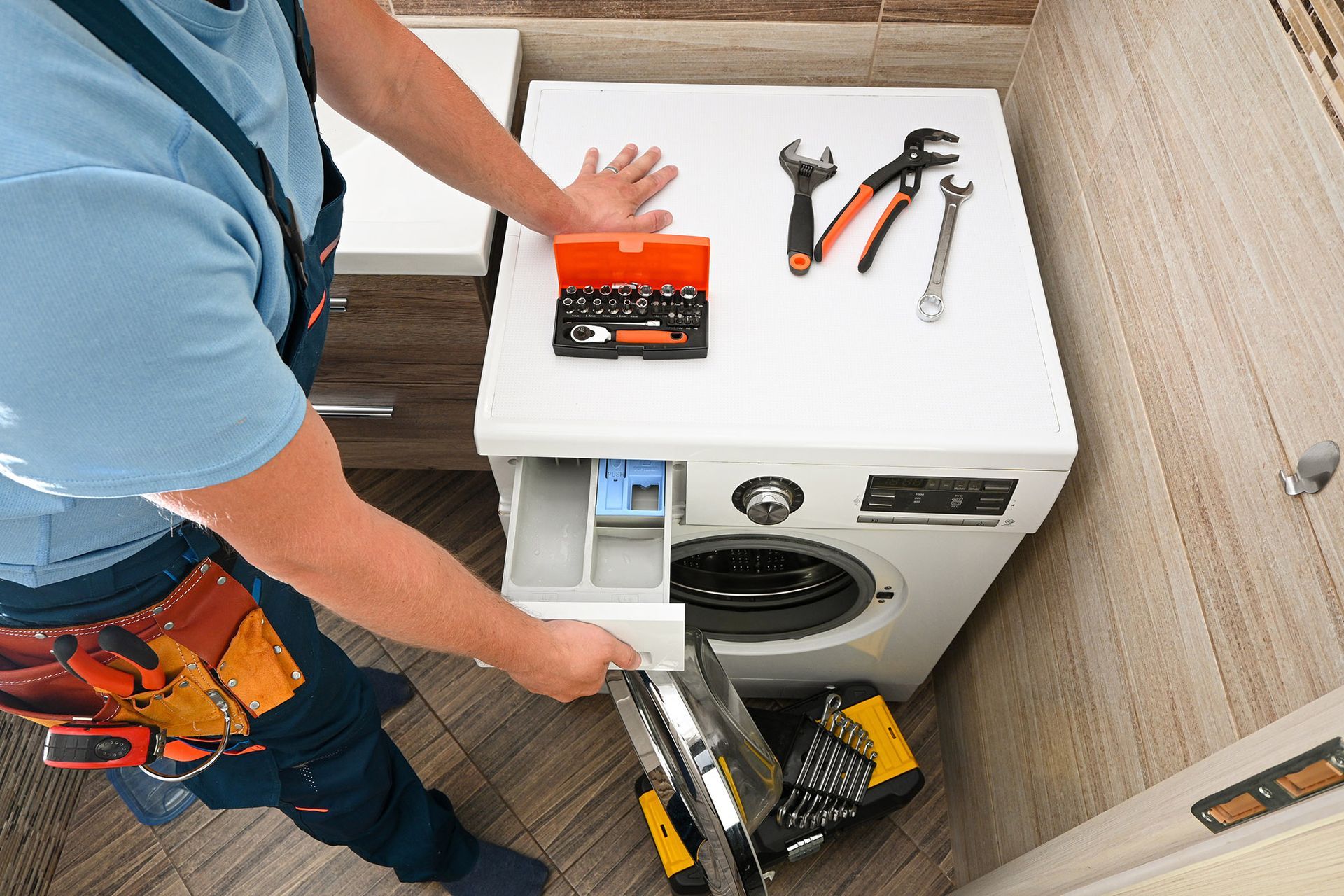 Person opening a washing machine's detergent drawer. Tools on top of the machine.