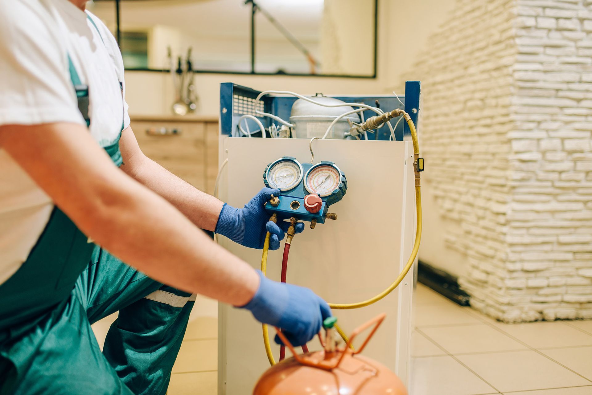 HVAC technician in blue gloves connects gauges to orange refrigerant tank.