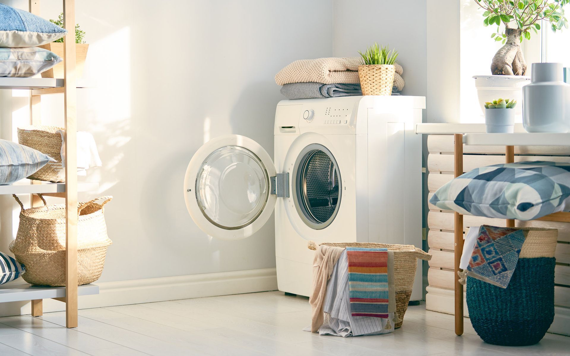 Washing machine with open door in a laundry room, light streaming in, towels and decor nearby.