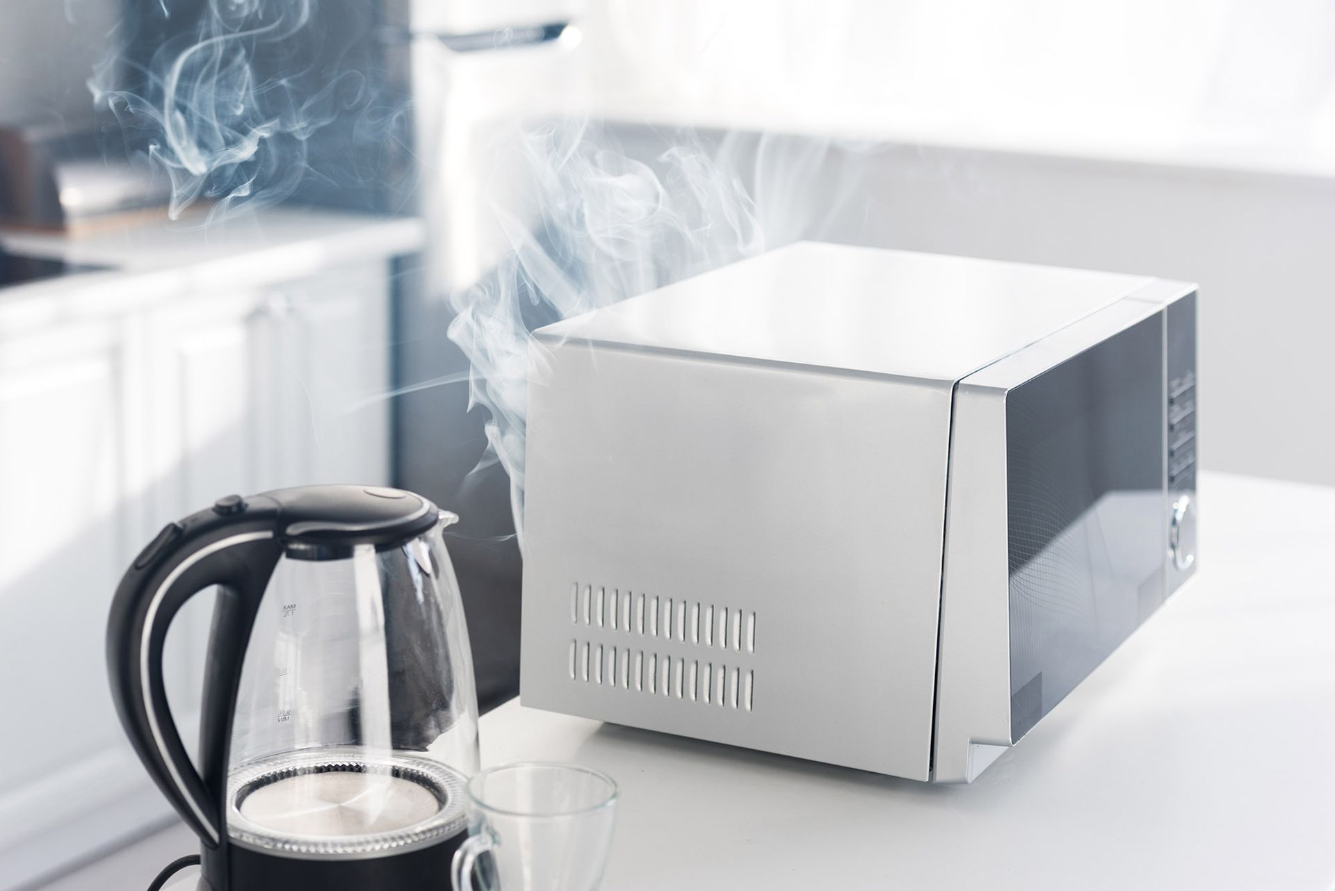 Smoke billowing from a microwave on a kitchen counter, next to a black electric kettle.