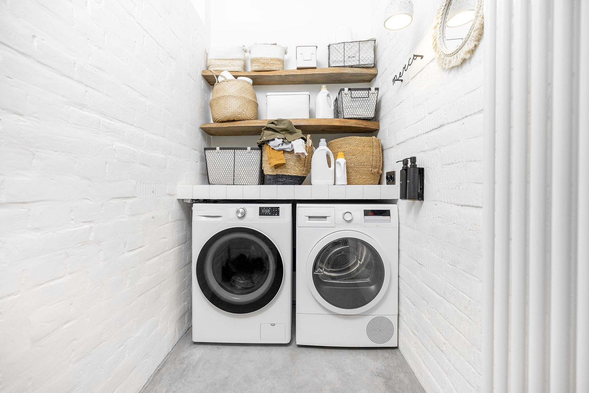 Laundry room with white washer and dryer, wooden shelves with baskets and supplies.