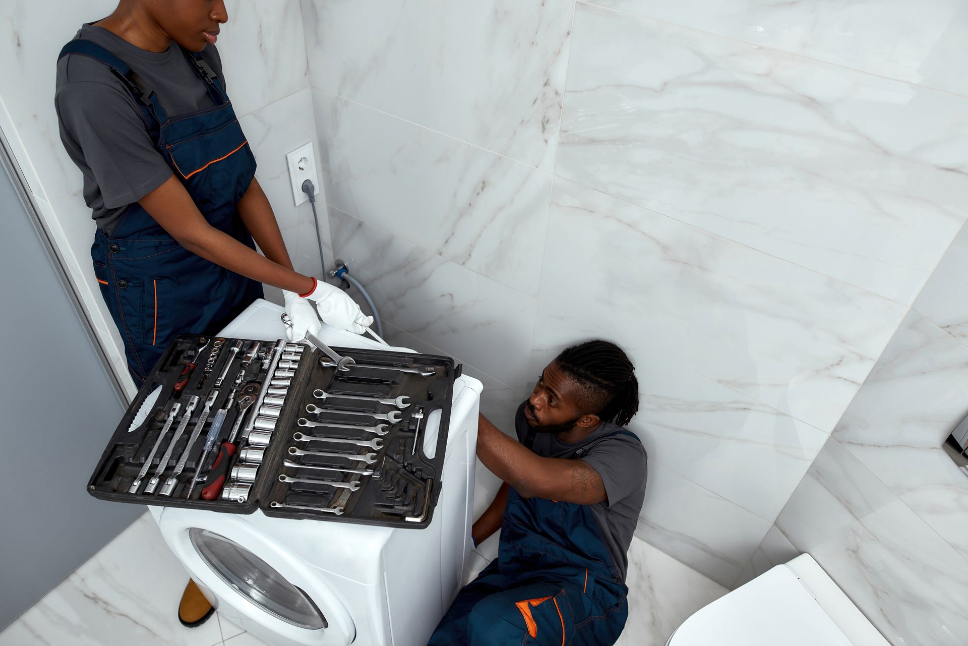 Man examines microwave with a flashlight in kitchen; toolbox nearby.