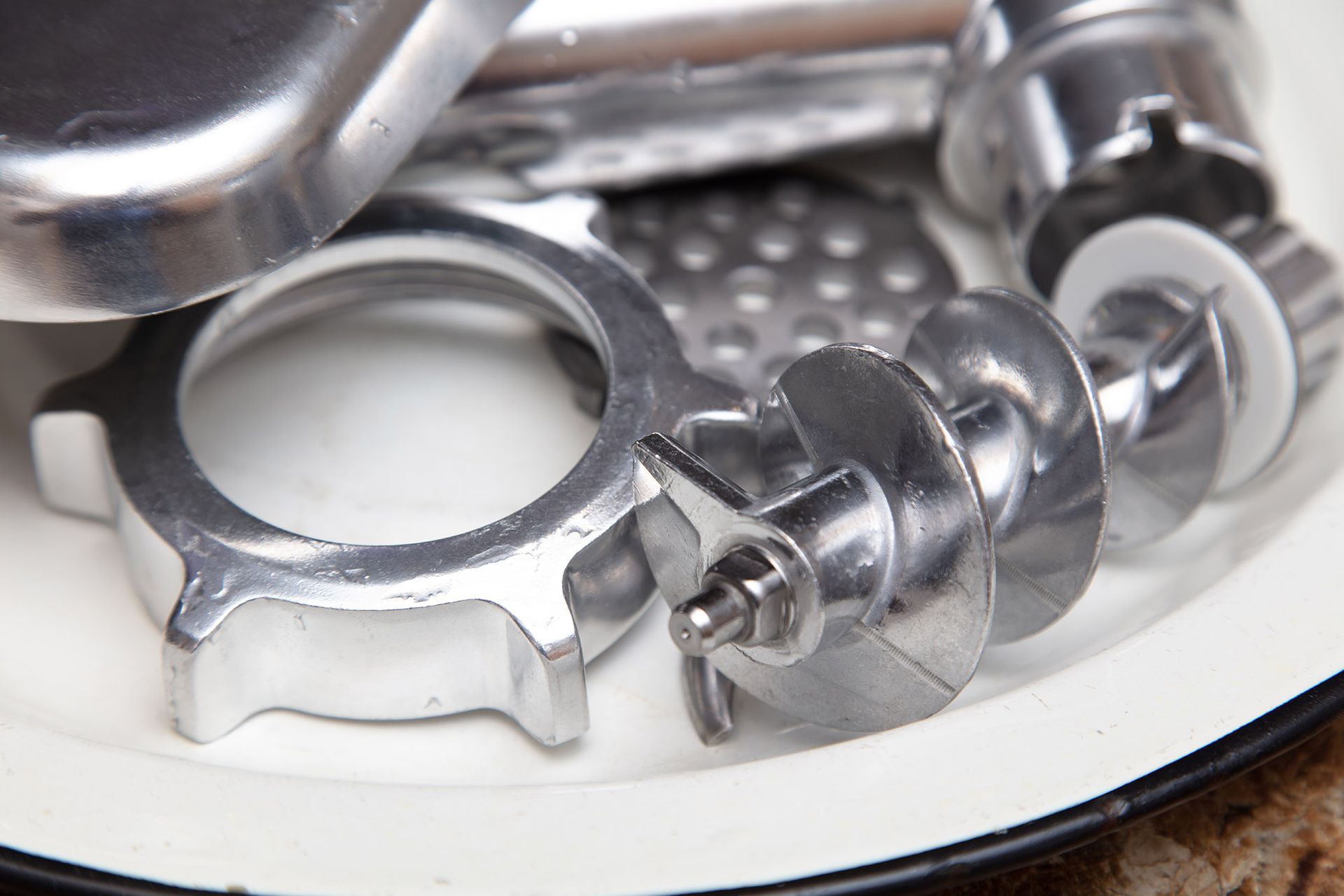 Metal meat grinder parts on a white plate, ready for assembly.