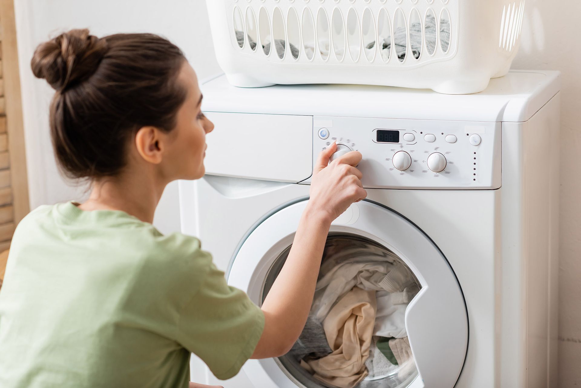 Woman setting washing machine dial, laundry basket on top.