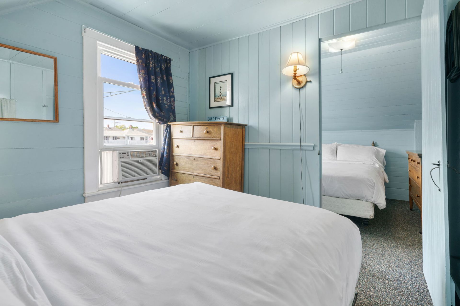 Bedroom with a bed, dresser, and a glimpse into an adjacent room. Light blue walls, white bedding.