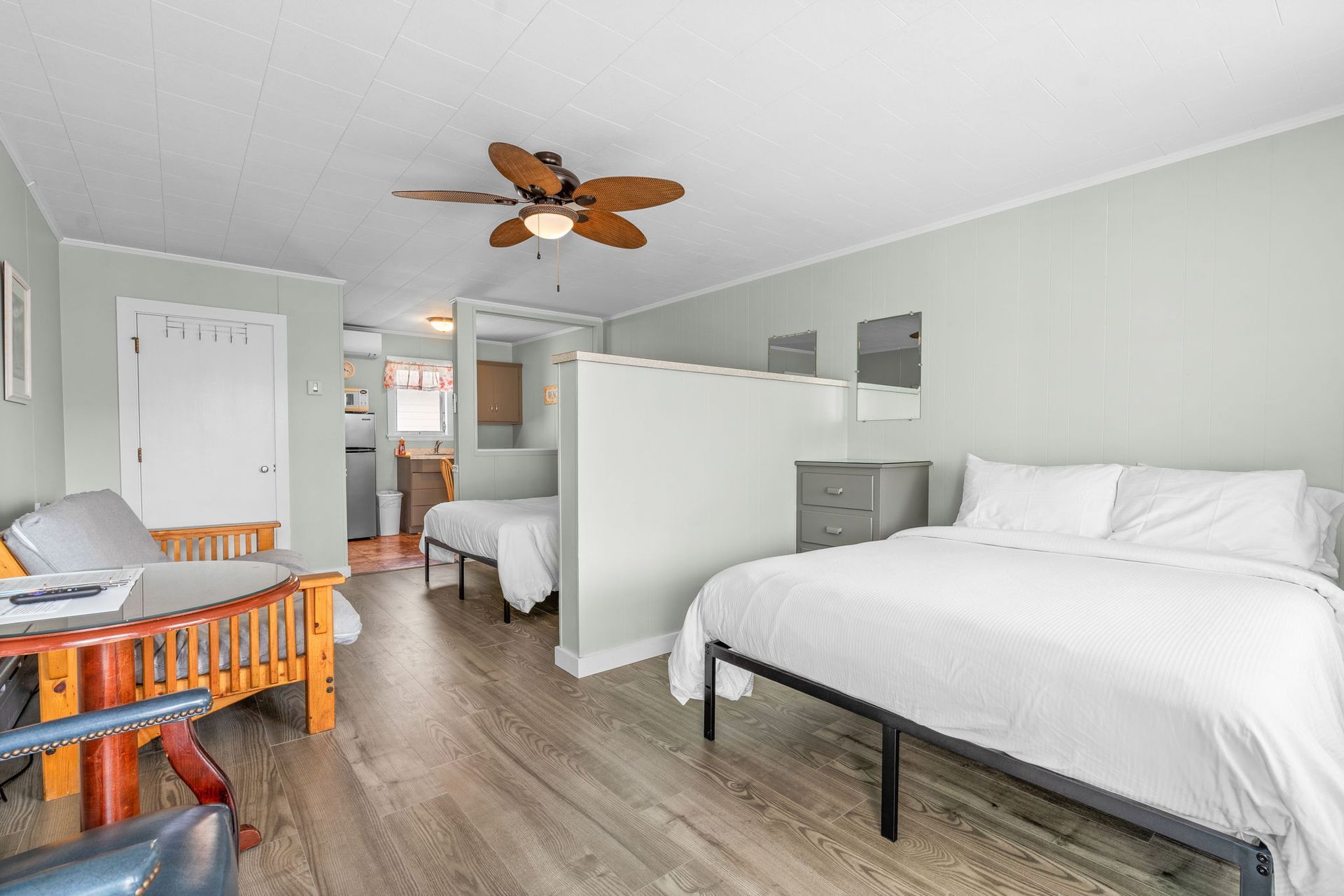 Studio apartment with two beds, kitchenette visible through doorway, grey walls.