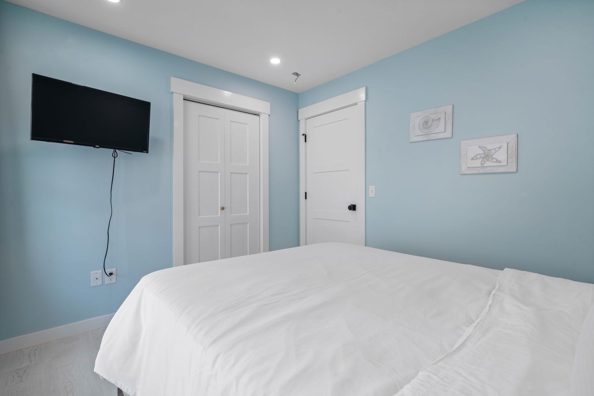 Bedroom with light blue walls, white bed, TV, closet, and door.