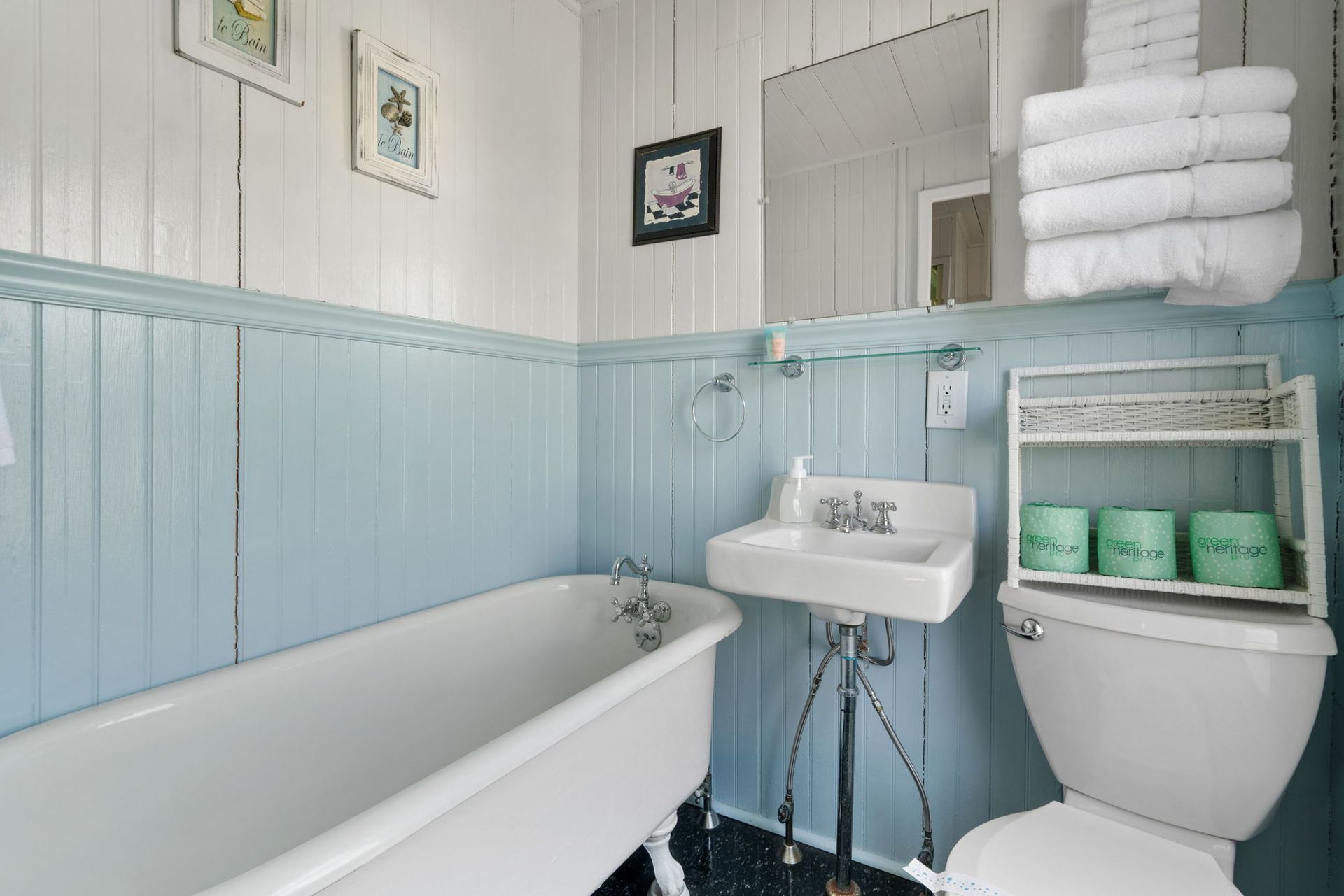 Bathroom with a white clawfoot tub, blue paneling, pedestal sink, and a stack of white towels.