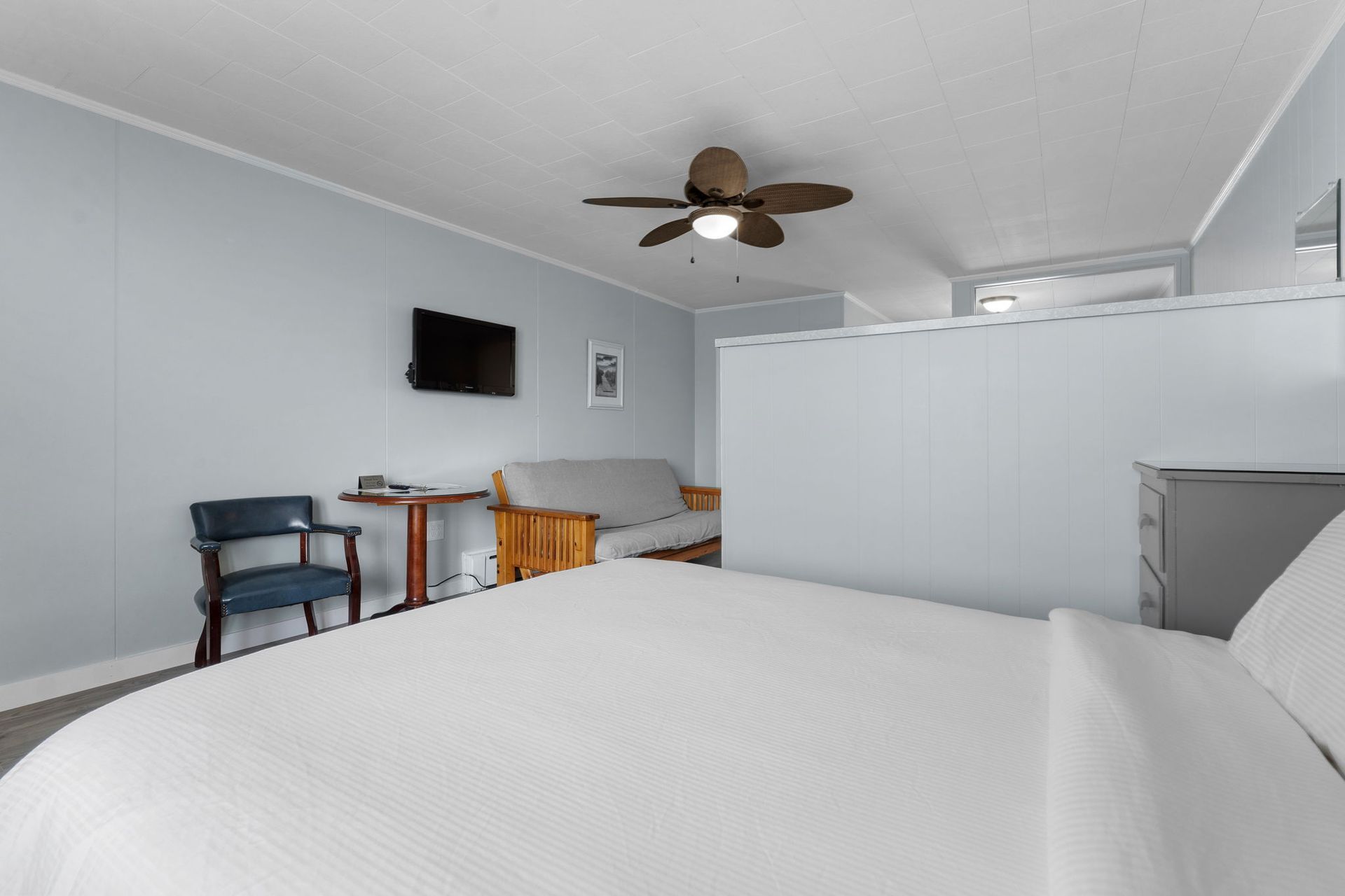 Small motel room with bed, futon, TV, desk, and blue walls.