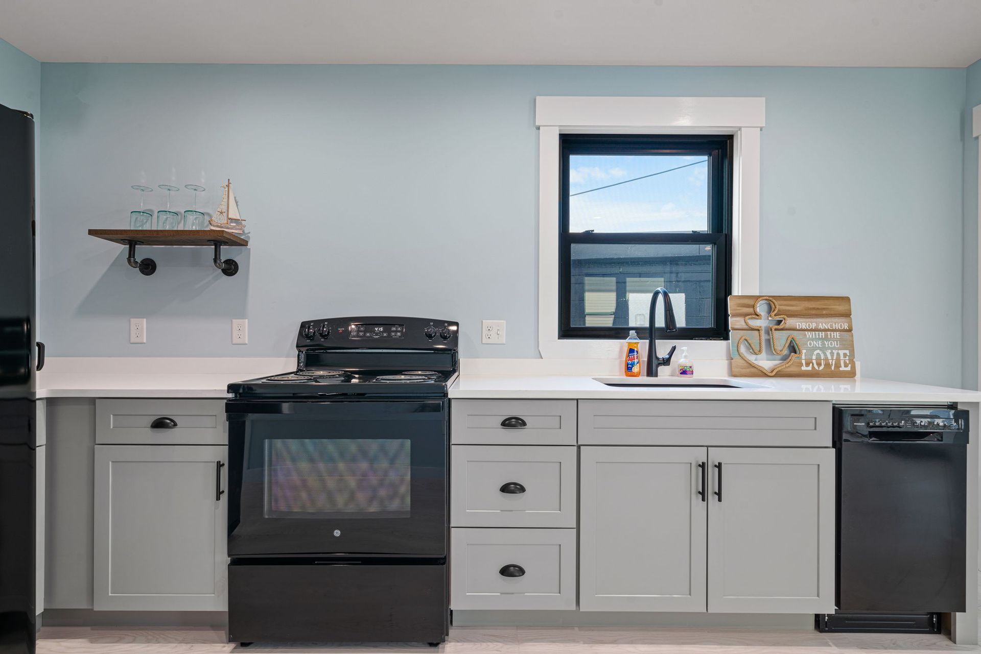 Kitchen with light gray cabinets, black appliances, white countertops, and a small window.