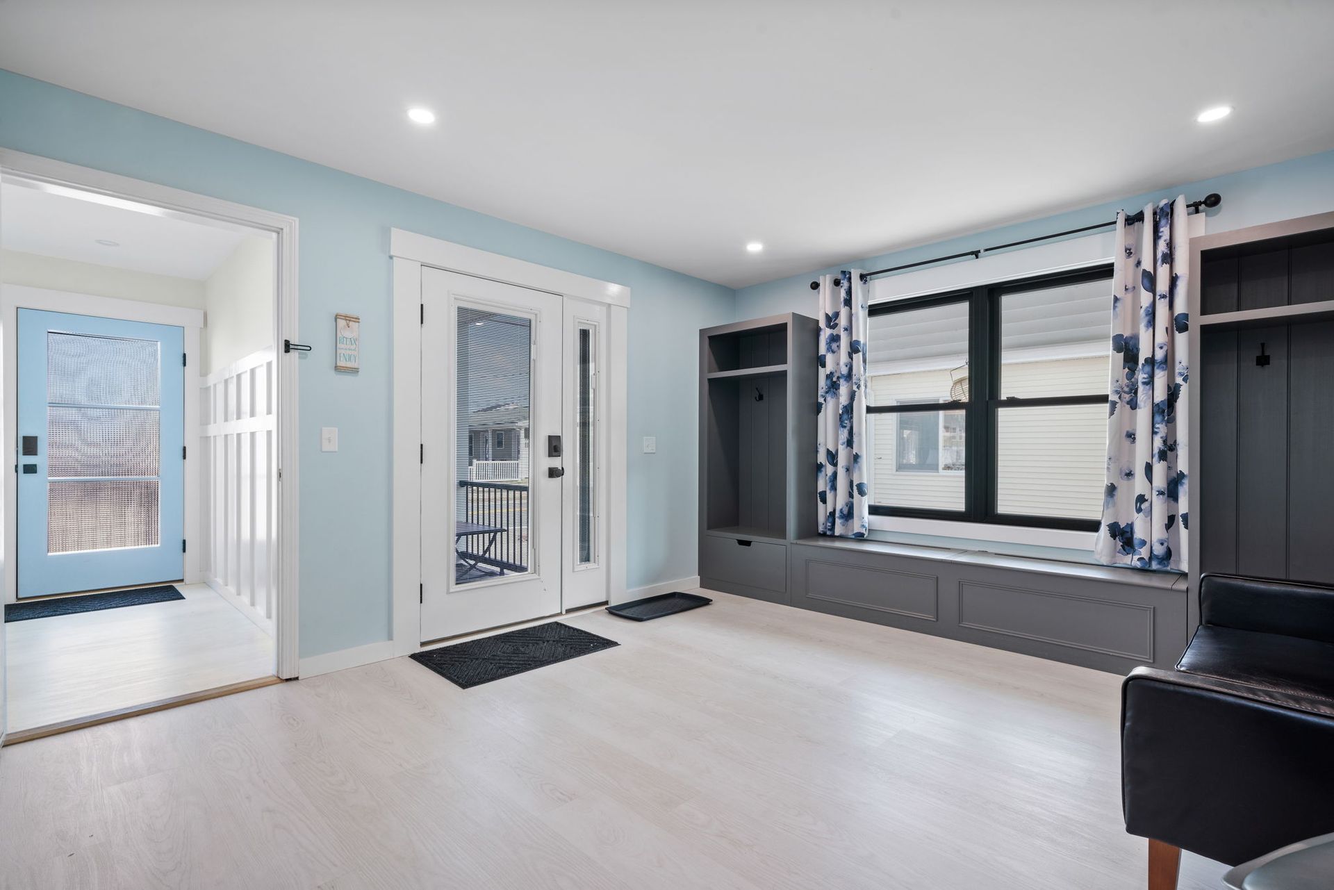 Entryway with light blue walls, white floor, front door, and built-in bench with storage and curtains.