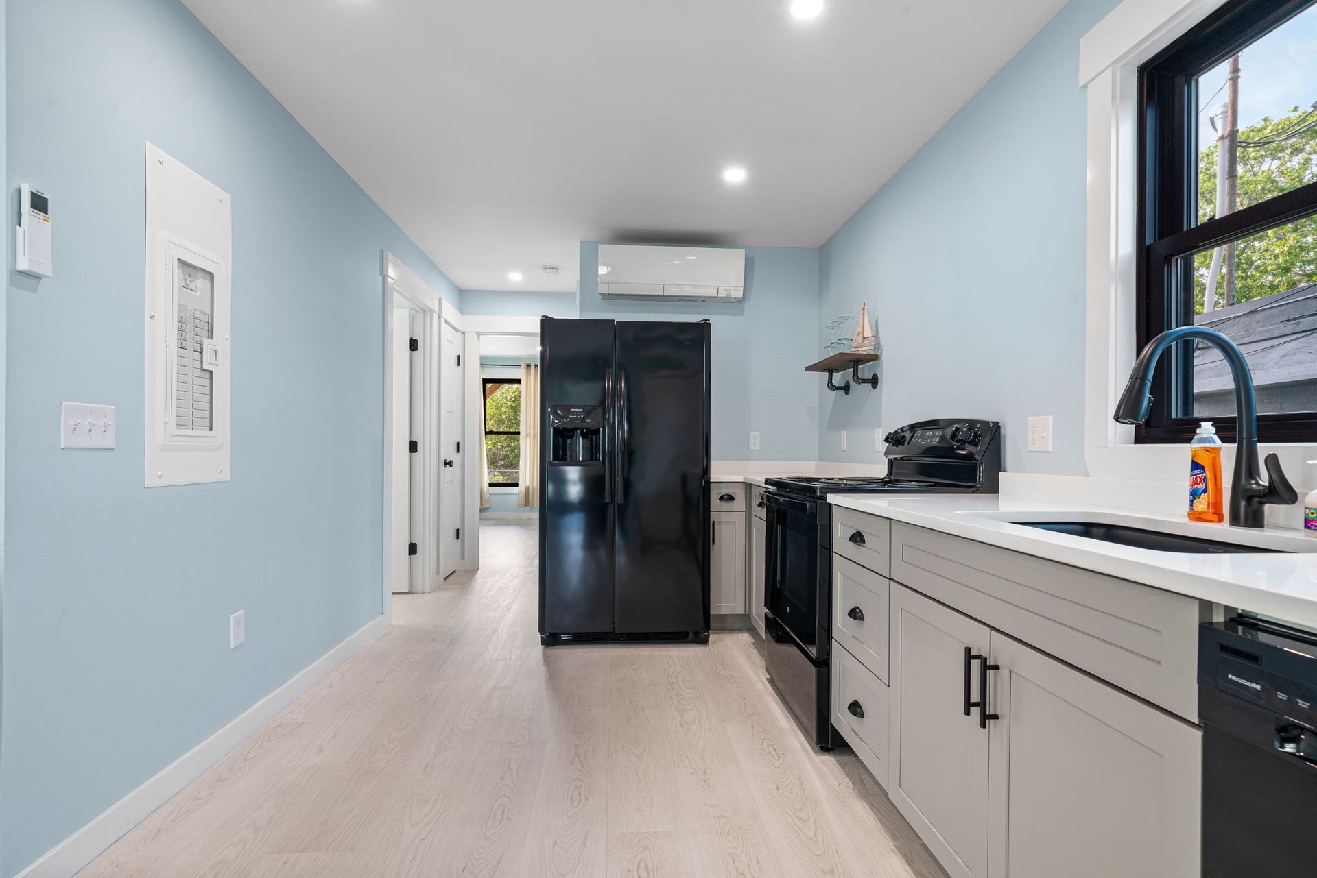 Light blue kitchen with black appliances, light cabinets, and wood-look flooring.